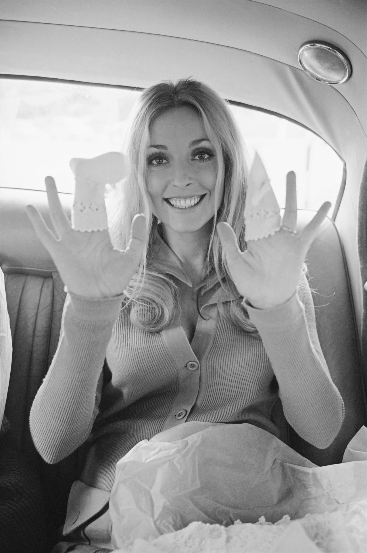 Sharon 桌布 壁紙 — 一位微笑的女士在復古車中舉起兩隻嬰兒鞋，同時看著相機。