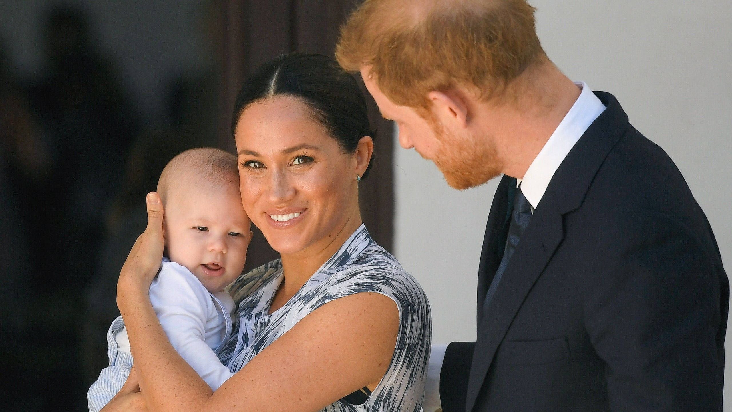 Meghan Markle 桌布 壁紙 — 一位微笑的女士抱著嬰兒，而一位穿西裝的男子靠近他們身邊。