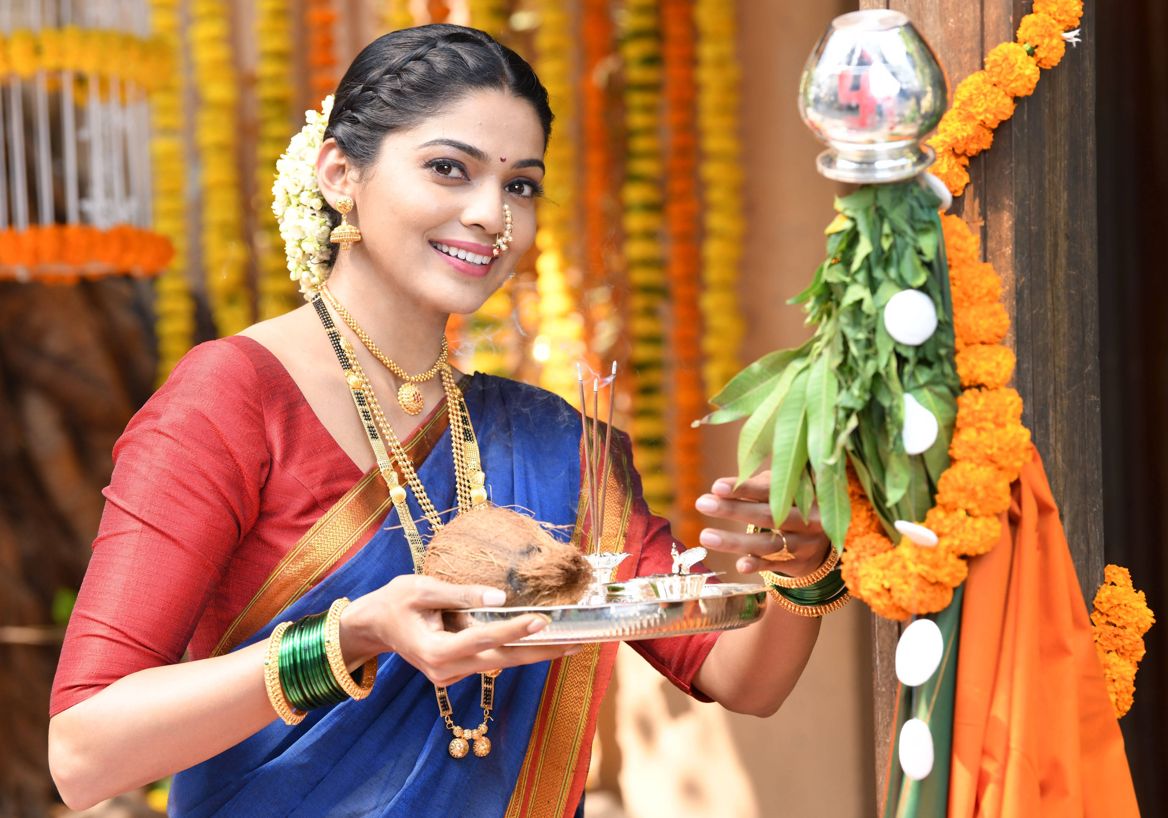 Gudi Padwa 桌布 壁紙 — 一位微笑的女士穿著傳統印度服裝，在節日儀式中手持一個托盤，上面有椰子和香，並以萬壽菊花環裝飾。