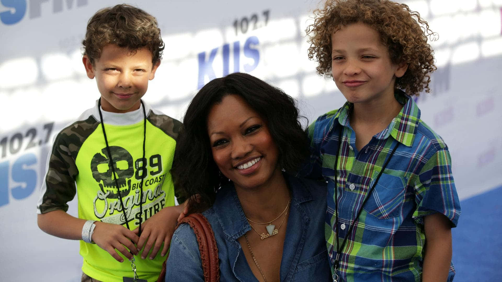 Garcelle Beauvais 桌布 壁紙 — 一位微笑的女士與兩名穿著彩色襯衫的小男孩在電台活動中一起擺姿勢。