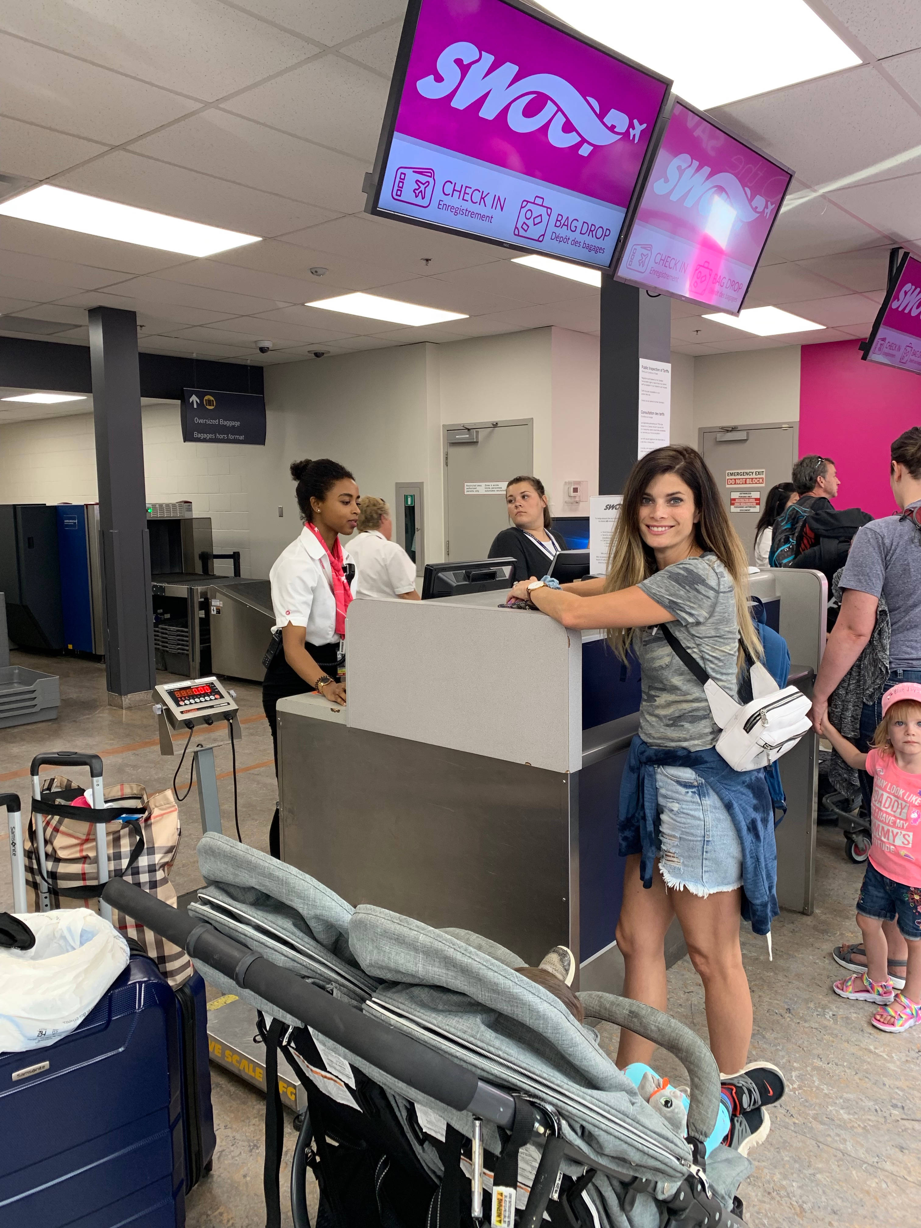 Aviation 桌布 壁紙 — 一位微笑的女士靠在SWOOP航空公司的報到櫃檯上，附近有嬰兒車和行李，工作人員正在協助旅客。