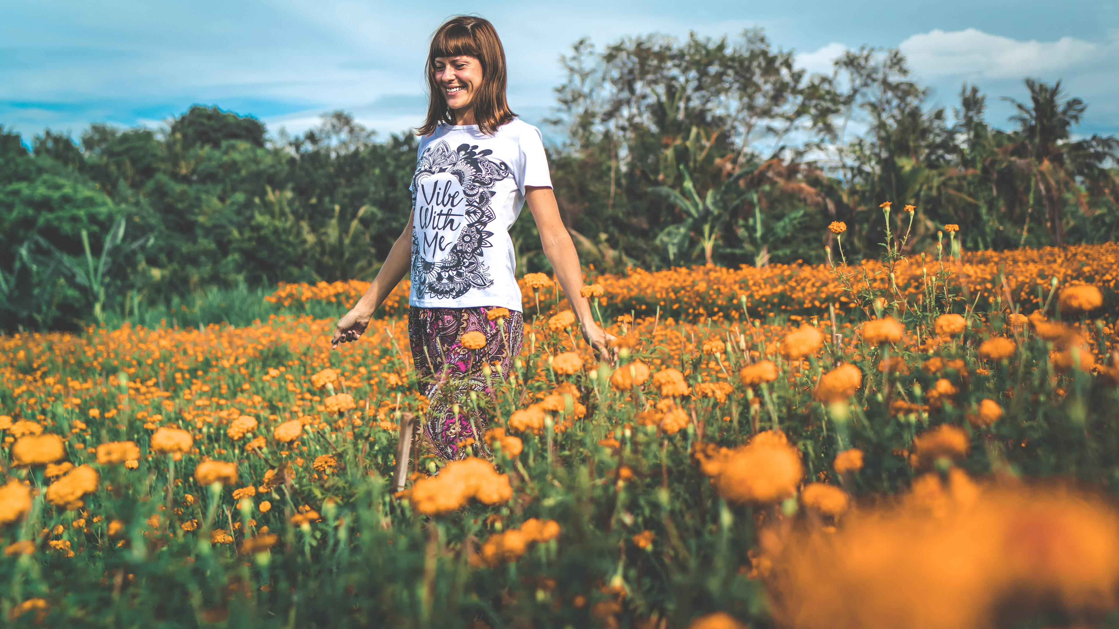 Marigold 桌布 壁紙 — 一位微笑的女子在晴朗的藍天下，愉快地走過一片充滿活力的橙色萬壽菊田野。