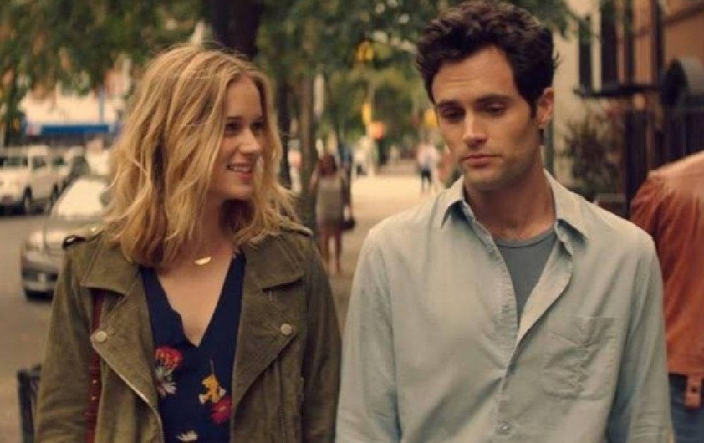 Netflix 桌布 壁紙 — 一位微笑的女子穿著綠色外套，與一位穿著淺色襯衫、沉思的男子並肩走在綠樹成蔭的城市街道上。