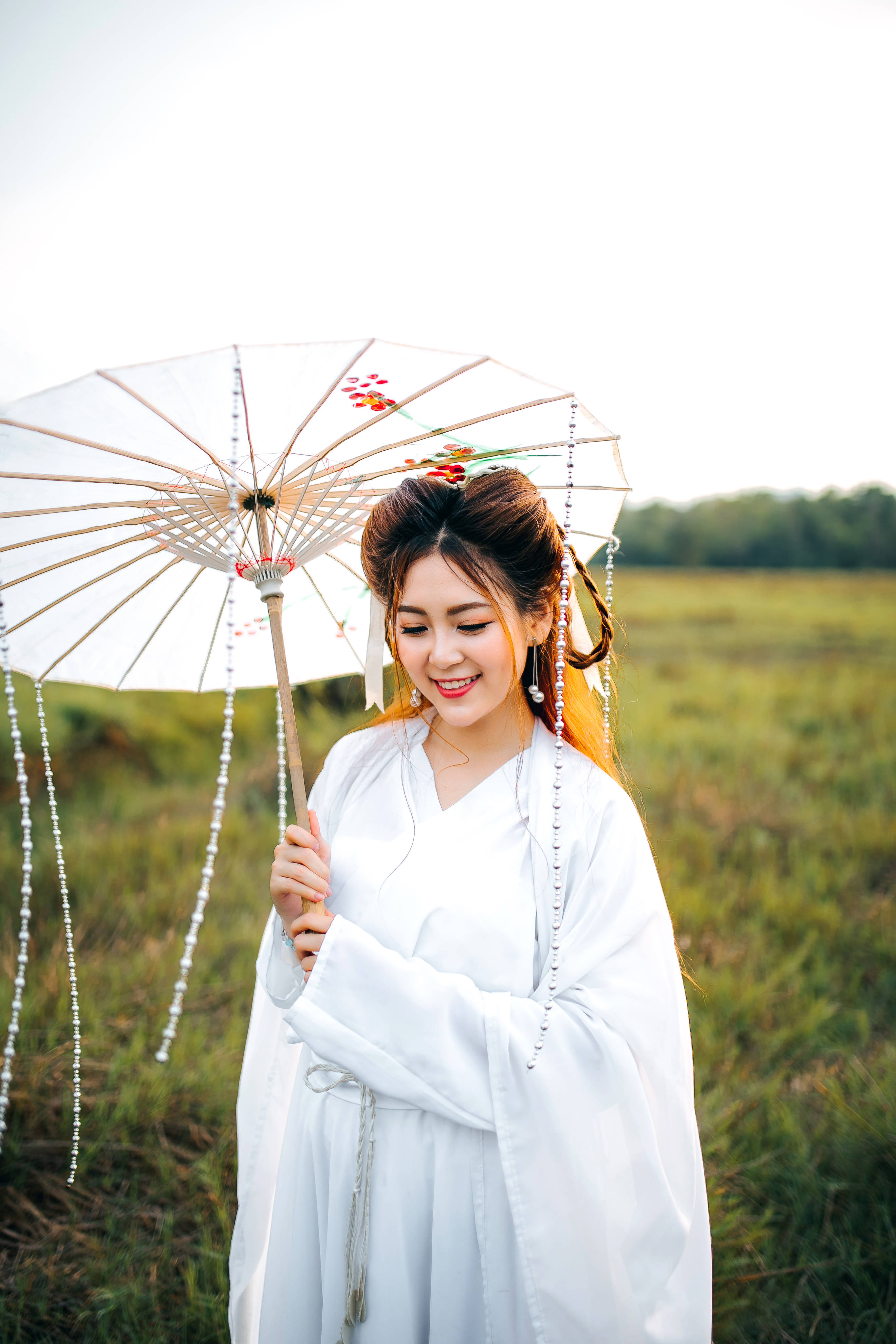 Woman 桌布 壁紙 — 一位微笑的女子身穿白色傳統長袍，在陽光照耀的草地上拿著一把裝飾性的陽傘。