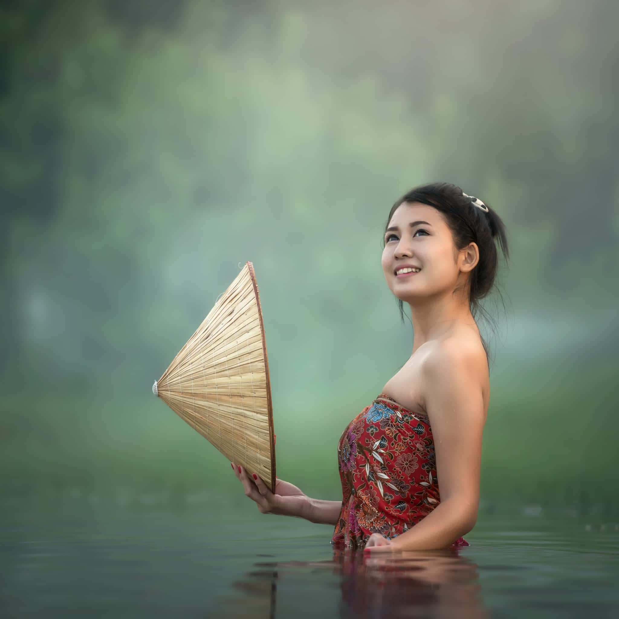 Beautiful Girls 桌布 壁紙 — 一位微笑的女子身穿紅色圖案連衣裙，站在及腰的霧水中，手持竹扇，身後是茂密的綠植。