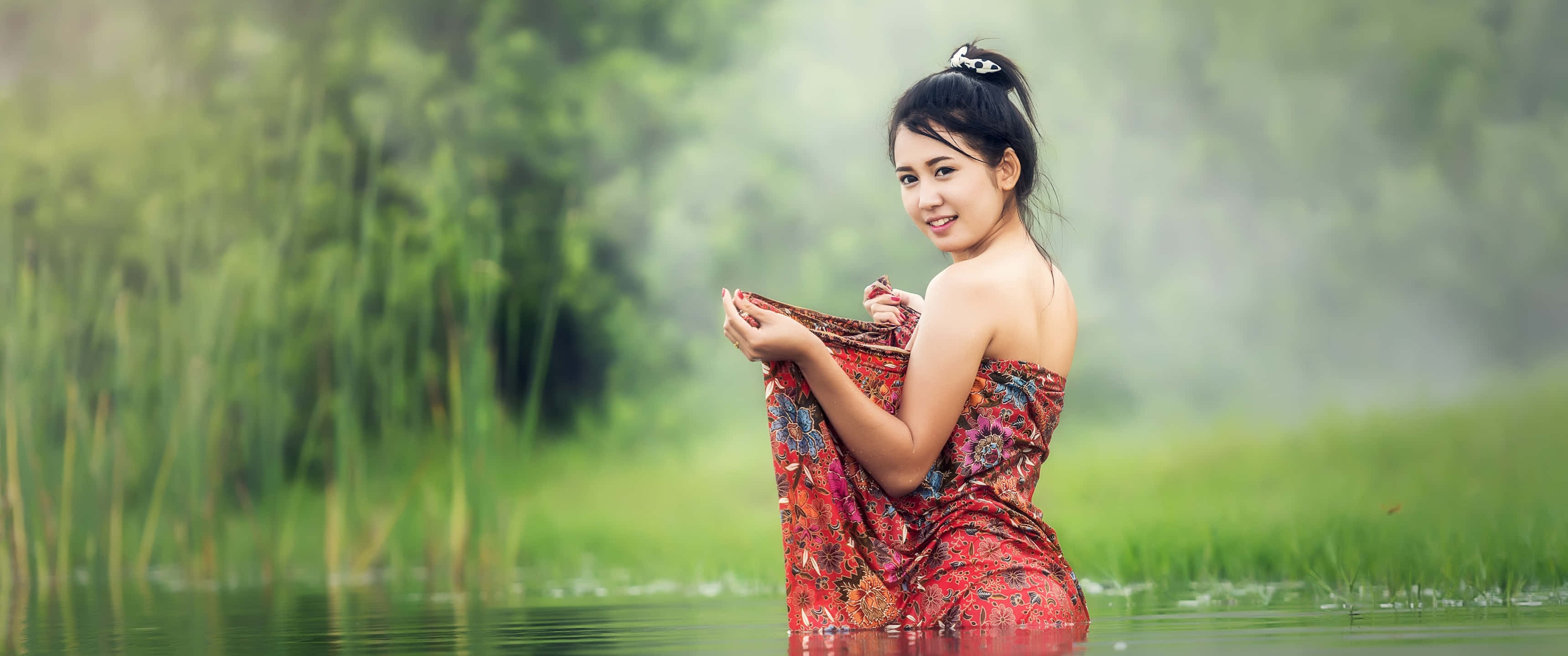 Beautiful Girls 桌布 壁紙 — 一位微笑的女子身穿紅色圖案連衣裙，站在被高蘆葦環繞的霧氣瀰漫的綠色池塘中，水深及腰。