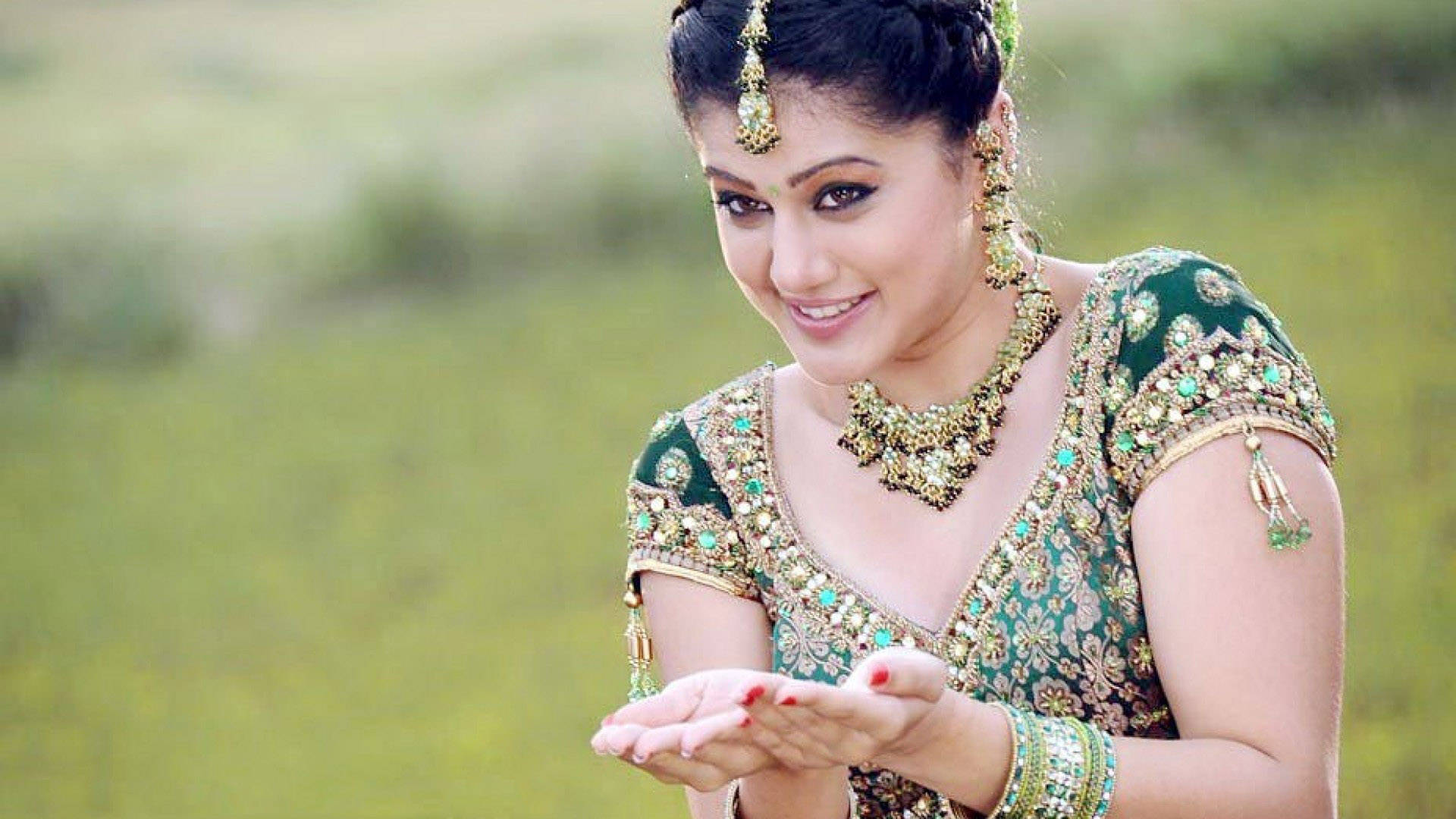 Taapsee Pannu 桌布 壁紙 — 一位微笑的女子身穿華麗的綠色傳統服飾，雙手張開，背景是柔和的模糊草地。