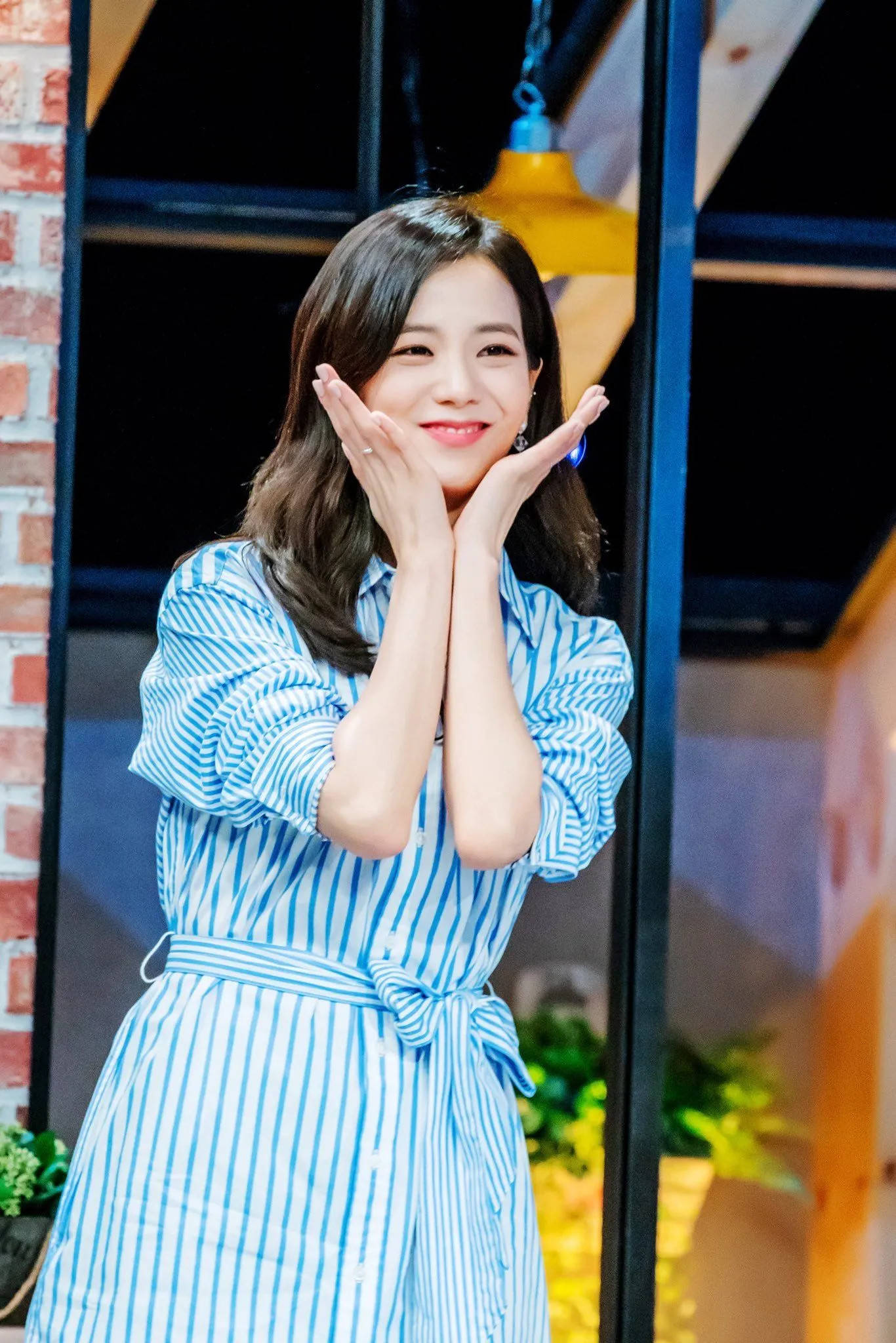 Jisoo Cute 桌布 壁紙 — 一位微笑的女子身穿藍色條紋連衣裙，雙手捧臉，背景是磚牆和吊燈。