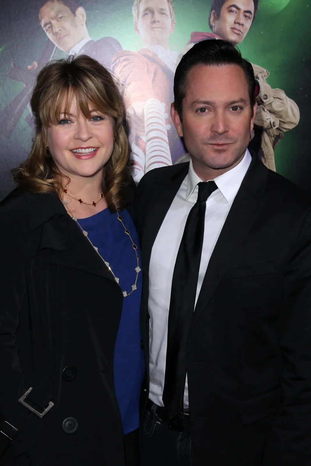 thomas lennon 桌布 壁紙 — 一位微笑的女子身穿黑色外套和藍色上衣，站在一位身穿黑色西裝和領帶的男子旁邊，出席電影首映禮。
