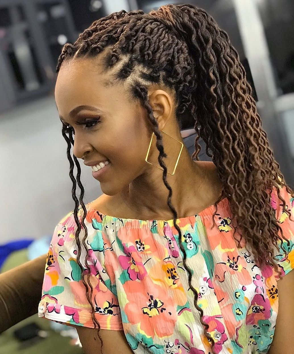 美女 桌布 壁紙 — 一位微笑的女性，擁有精緻辮子頭髮和幾何耳環，穿著鮮豔的花卉上衣。
