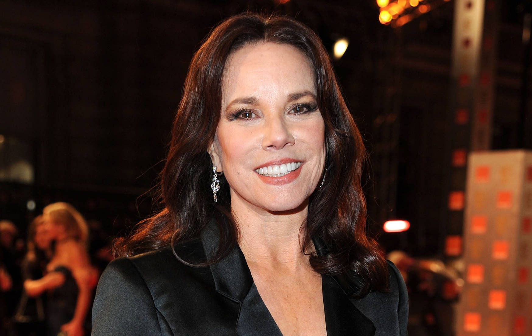 Celebrity 桌布 壁紙 — 一位微笑的女性，深色波浪長髮，戴著優雅耳環，在華麗的晚間活動中穿著黑色西裝外套。