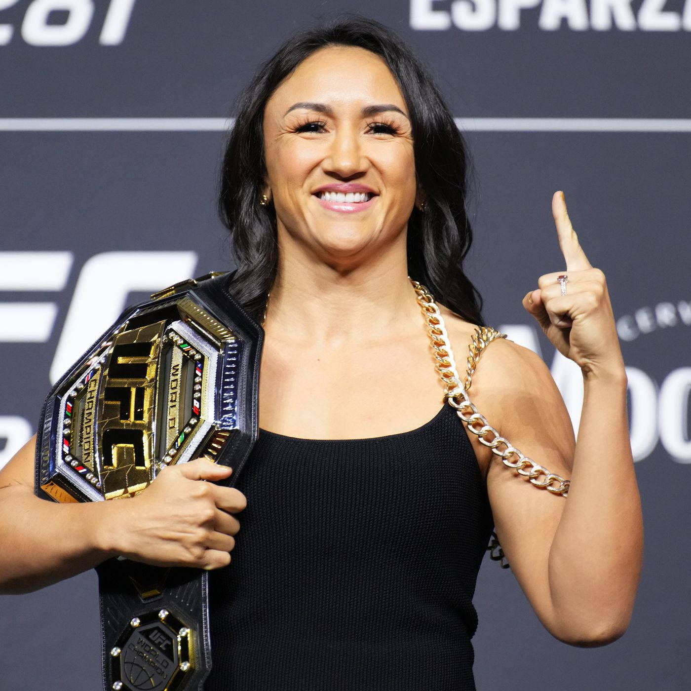 Champion 桌布 壁紙 — 一位微笑的女性UFC冠軍自豪地舉起她的冠軍腰帶，並自信地向上指。