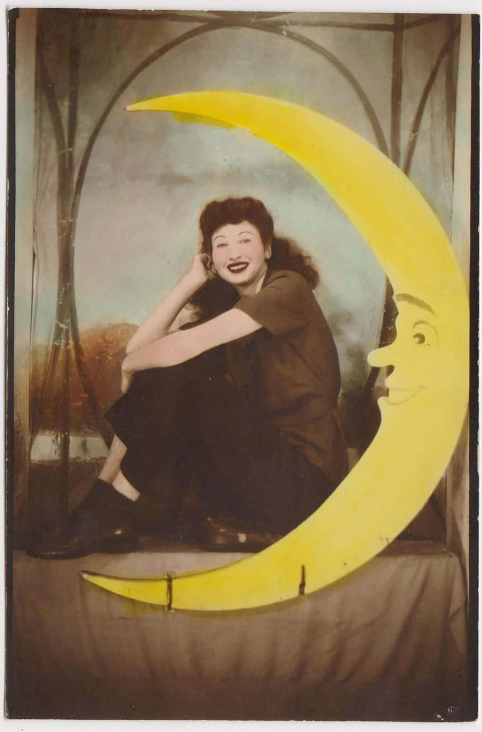Moon Face 桌布 壁紙 — 一位微笑的女性在復古工作室場景中，俏皮地站在一個大型黃色新月形剪紙旁擺姿勢。