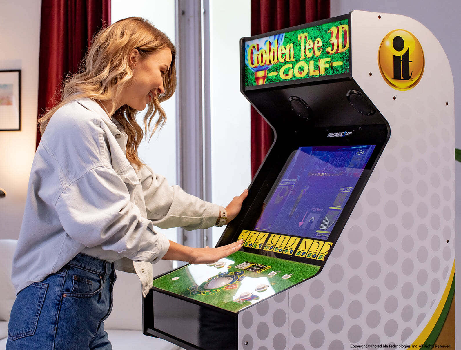Arcade Games 桌布 壁紙 — 一位微笑的女性在明亮的街機上玩 Golden Tee 3D Golf，置身舒適的室內環境。
