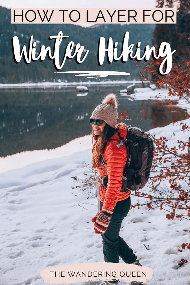 Winter Hiking 桌布 壁紙 — 一位微笑的女性穿著亮橙色外套和粉紅色毛帽，在雪地中健行，旁邊是平靜、覆蓋薄雪的湖泊，背景是樹木繁茂的山丘。