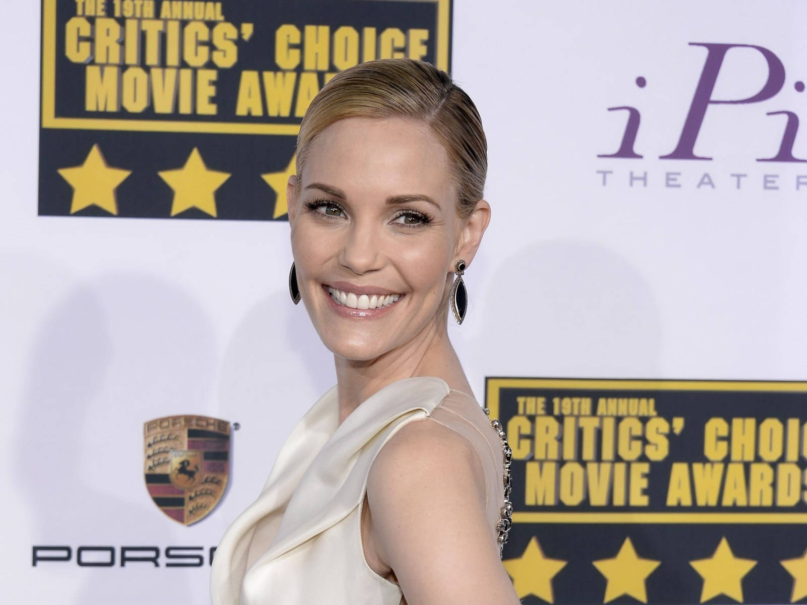 Celebrity 桌布 壁紙 — 一位微笑的女性穿著奶油色禮服在評論家選擇電影獎上擺姿勢，身後有保時捷和iPic Theater的標誌。