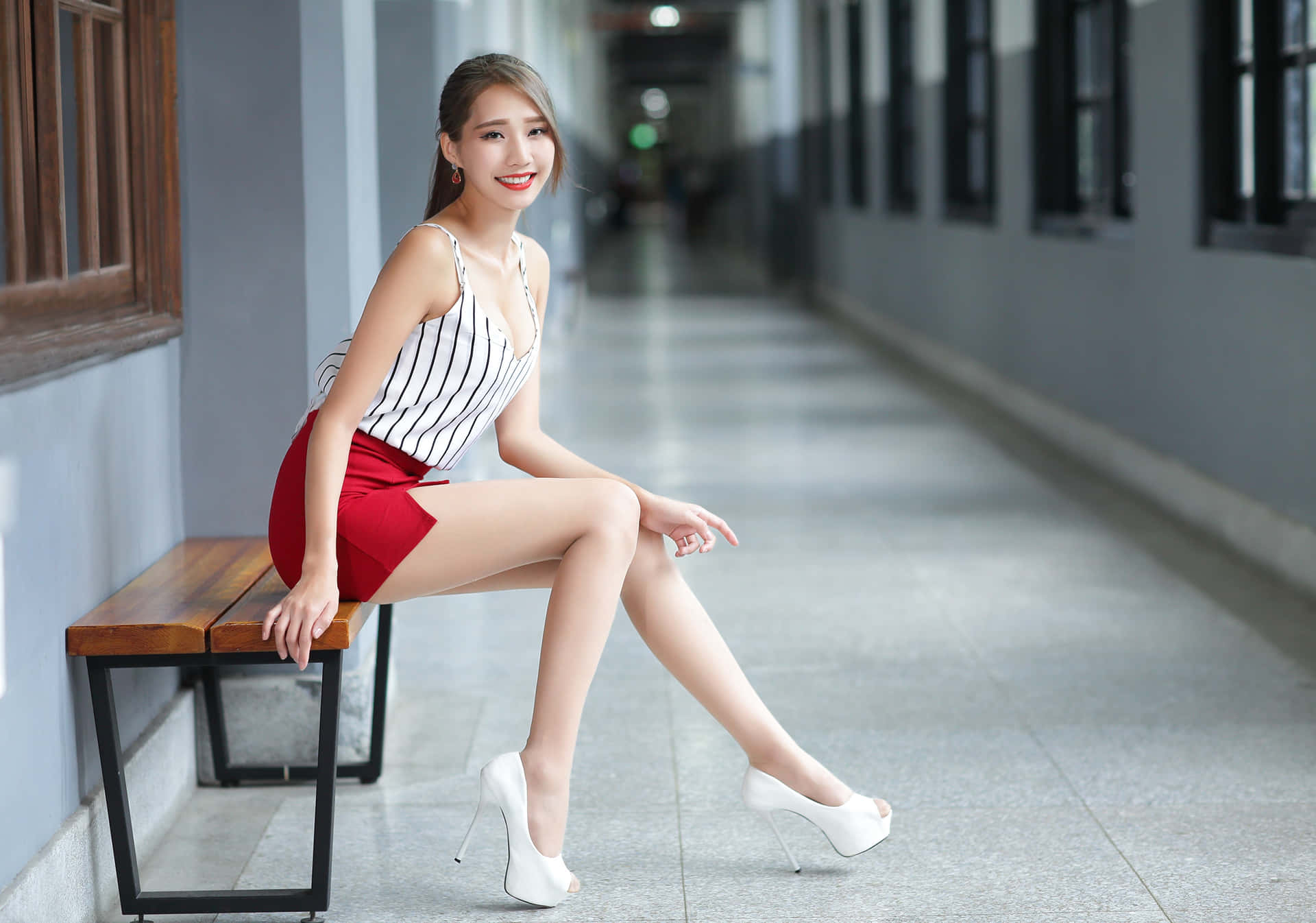 穿著紅色短褲和白色高跟鞋的女性坐在走廊的長椅上。 — 少女風 GIF 壁紙
