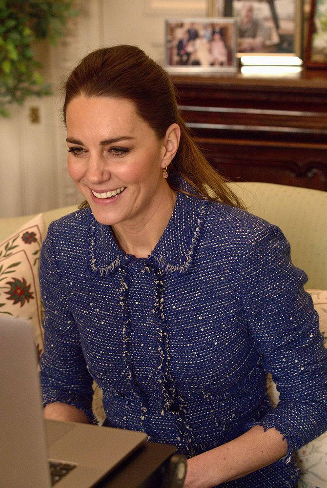 Kate Middleton 桌布 壁紙 — 一位微笑的女性穿著質感藍色外套，坐在書桌前使用筆記型電腦，室內光線溫暖。