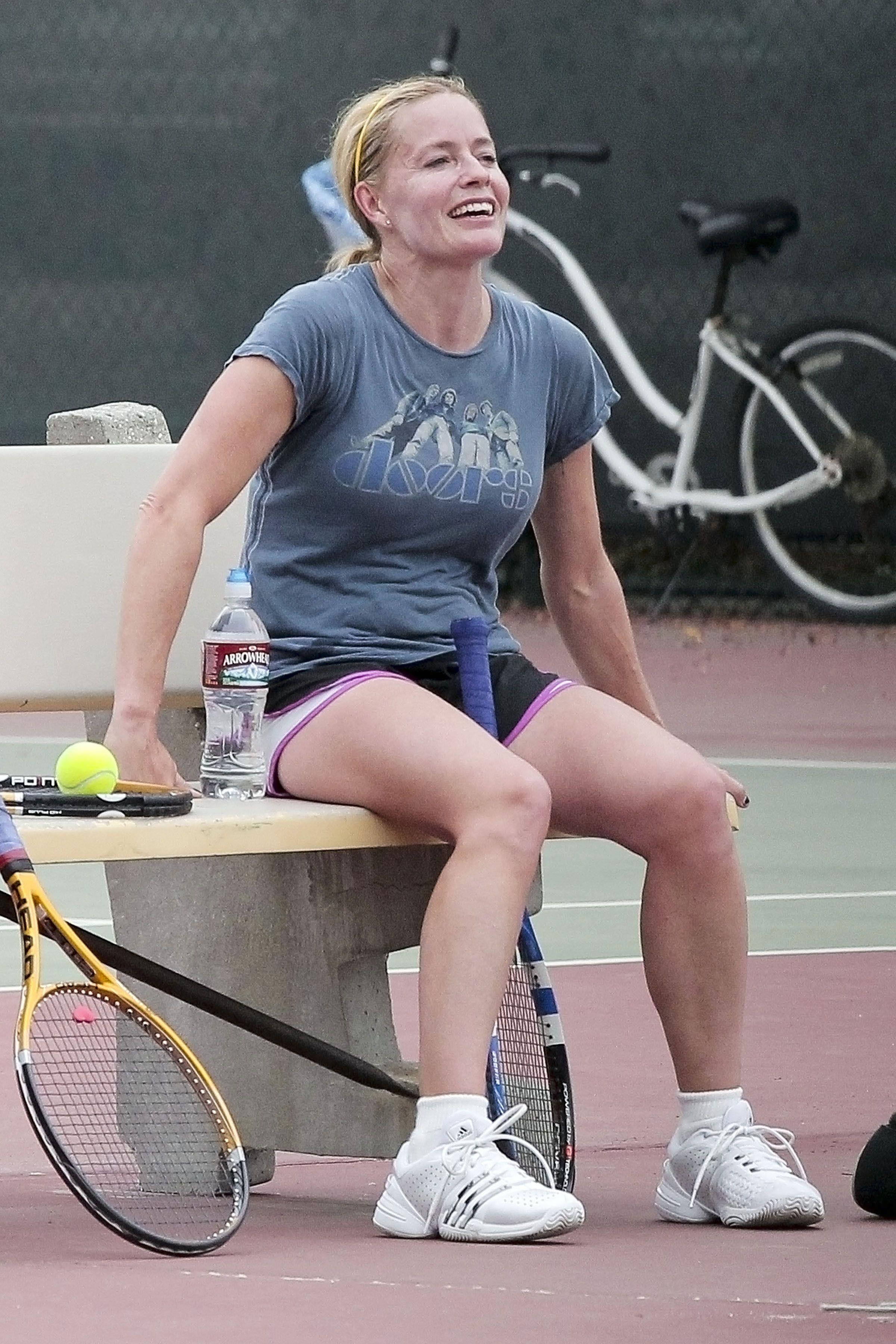 Tennis 桌布 壁紙 — 一位微笑的女性穿著運動裝備，坐在網球場的長椅上大笑，旁邊放著球拍和水瓶。