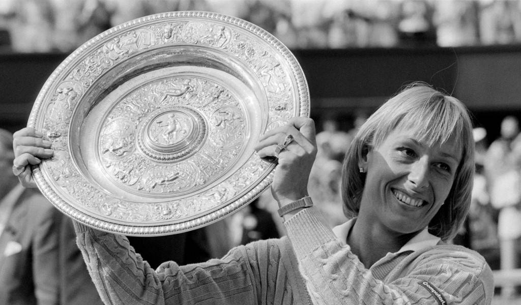 Martina Navratilova 桌布 壁紙 — 一位微笑的女性自豪地高舉一個大型華麗的銀色網球獎盃，背景是模糊的人群。