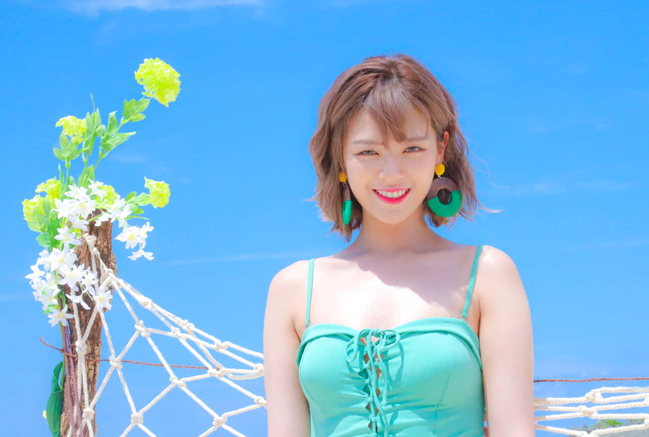 twice 桌布 壁紙 — 一位微笑的女性身穿青綠色泳衣，站在明亮的藍天下，旁邊是一個花卉網狀柱子。
