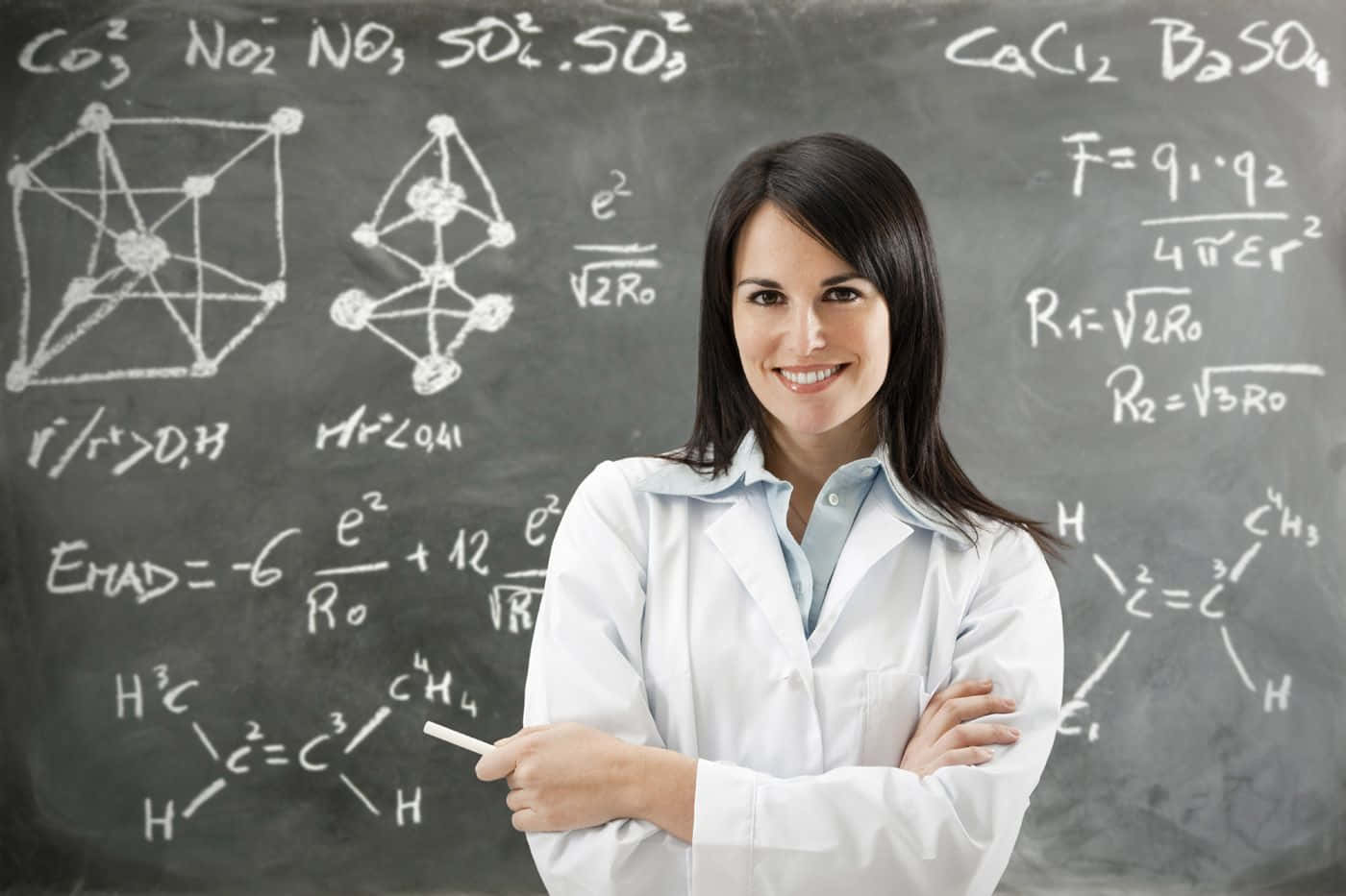 teachers 桌布 壁紙 — 一位微笑的女科學家身穿白色實驗室外套，自信地站在充滿複雜化學公式和分子結構的黑板前。