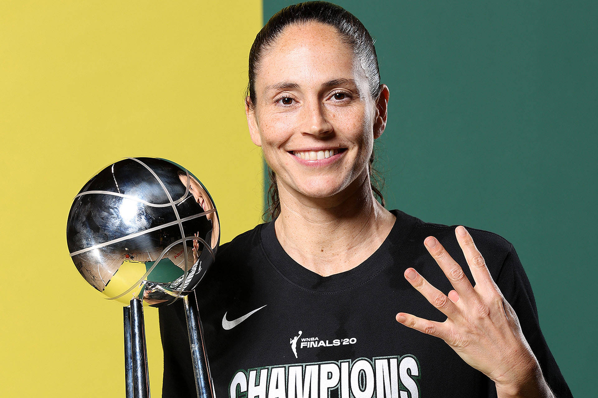 Sue 桌布 壁紙 — 一位微笑的女籃球員身穿黑色「Champions」球衣，在黃綠分割的背景前高舉閃亮的銀色獎盃。