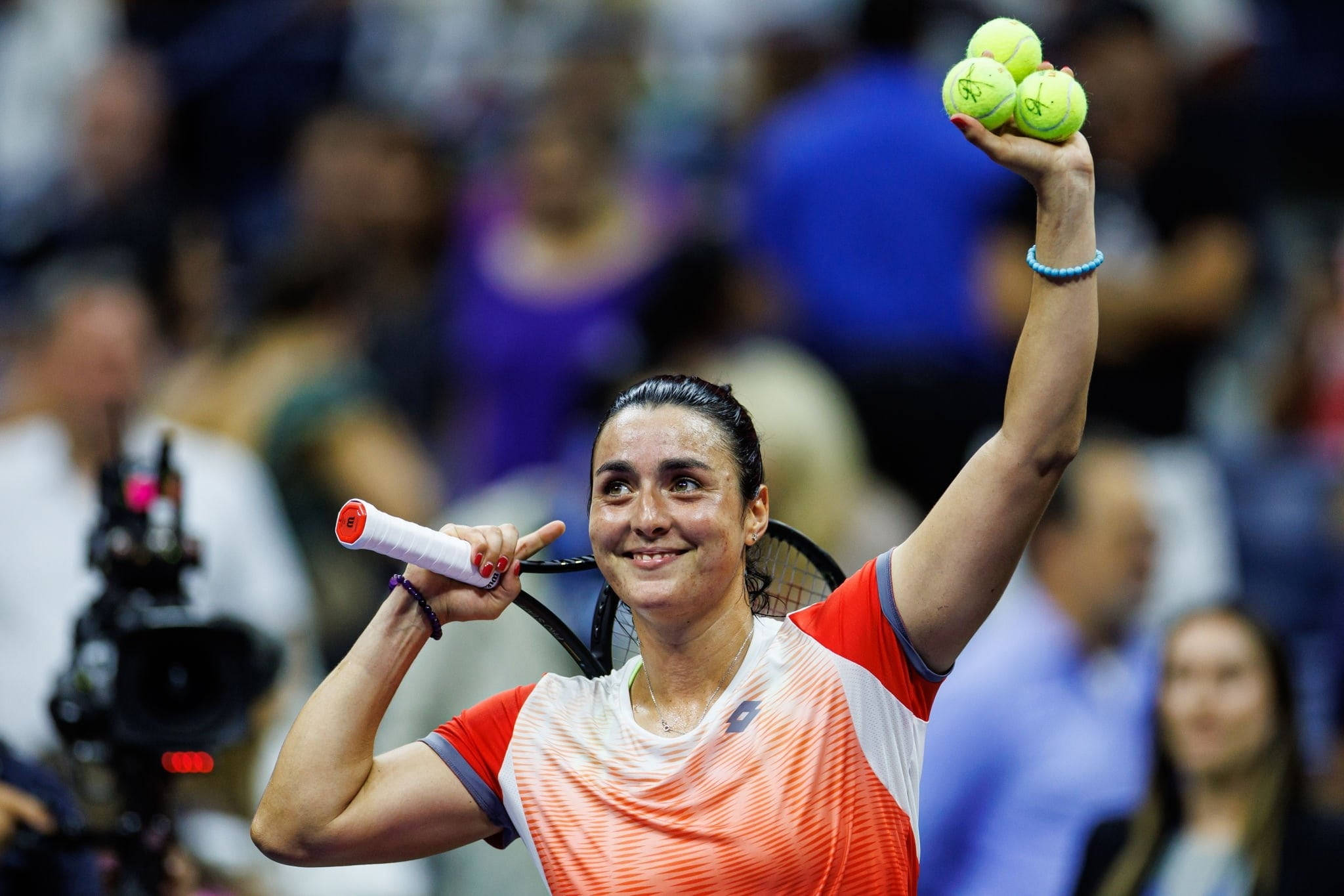 Athlete 桌布 壁紙 — 一位微笑的女網球運動員在燈光明亮的體育場中高舉三個網球慶祝勝利。