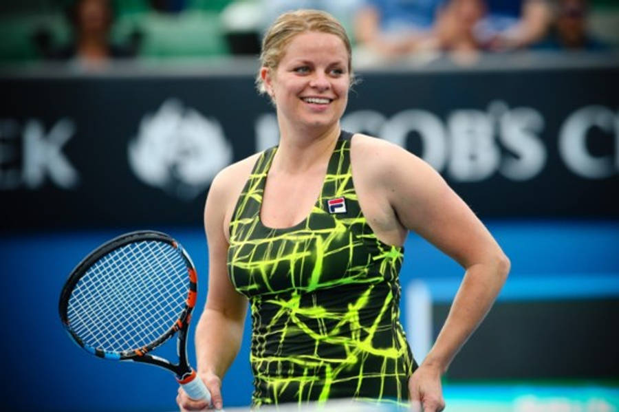 Tennis 桌布 壁紙 — 一位微笑的女網球運動員穿著螢光綠和黑色連衣裙，在藍色球場上握著球拍，身後有模糊的觀眾。
