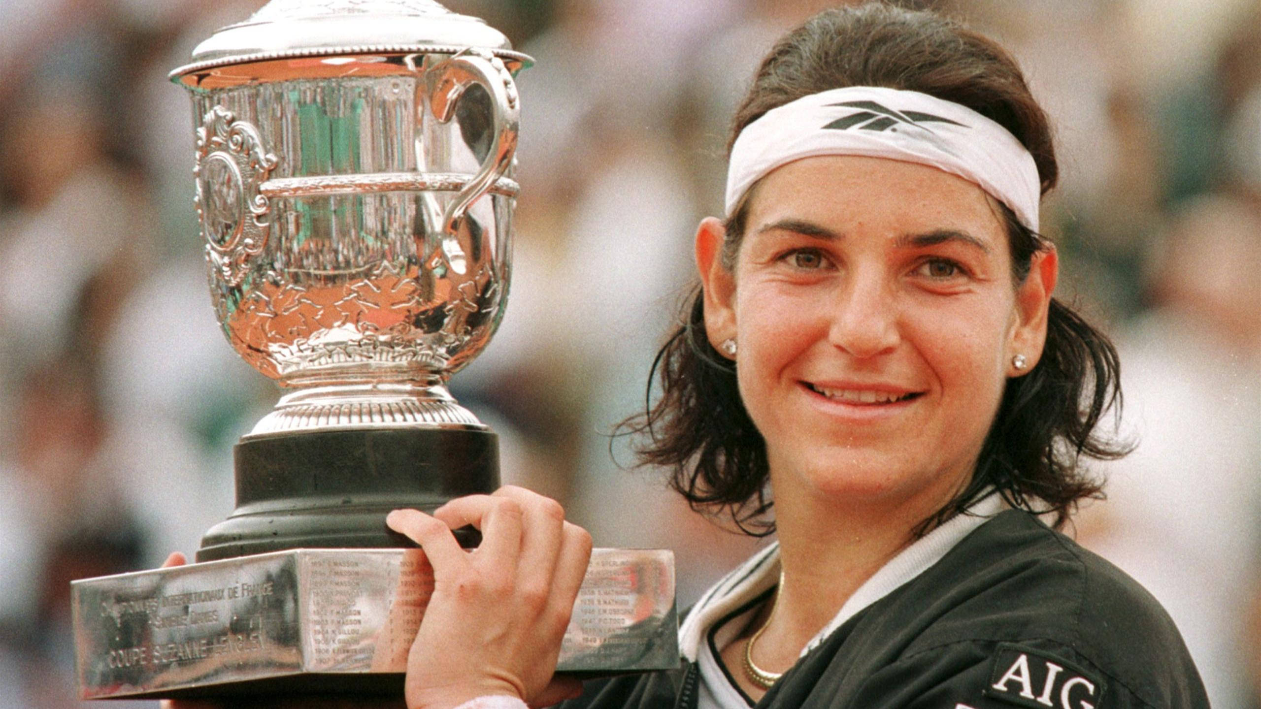 Tennis 桌布 壁紙 — 一位微笑的女網球運動員自豪地高舉一個刻有細節的大型銀色獎盃，背景是模糊的人群。