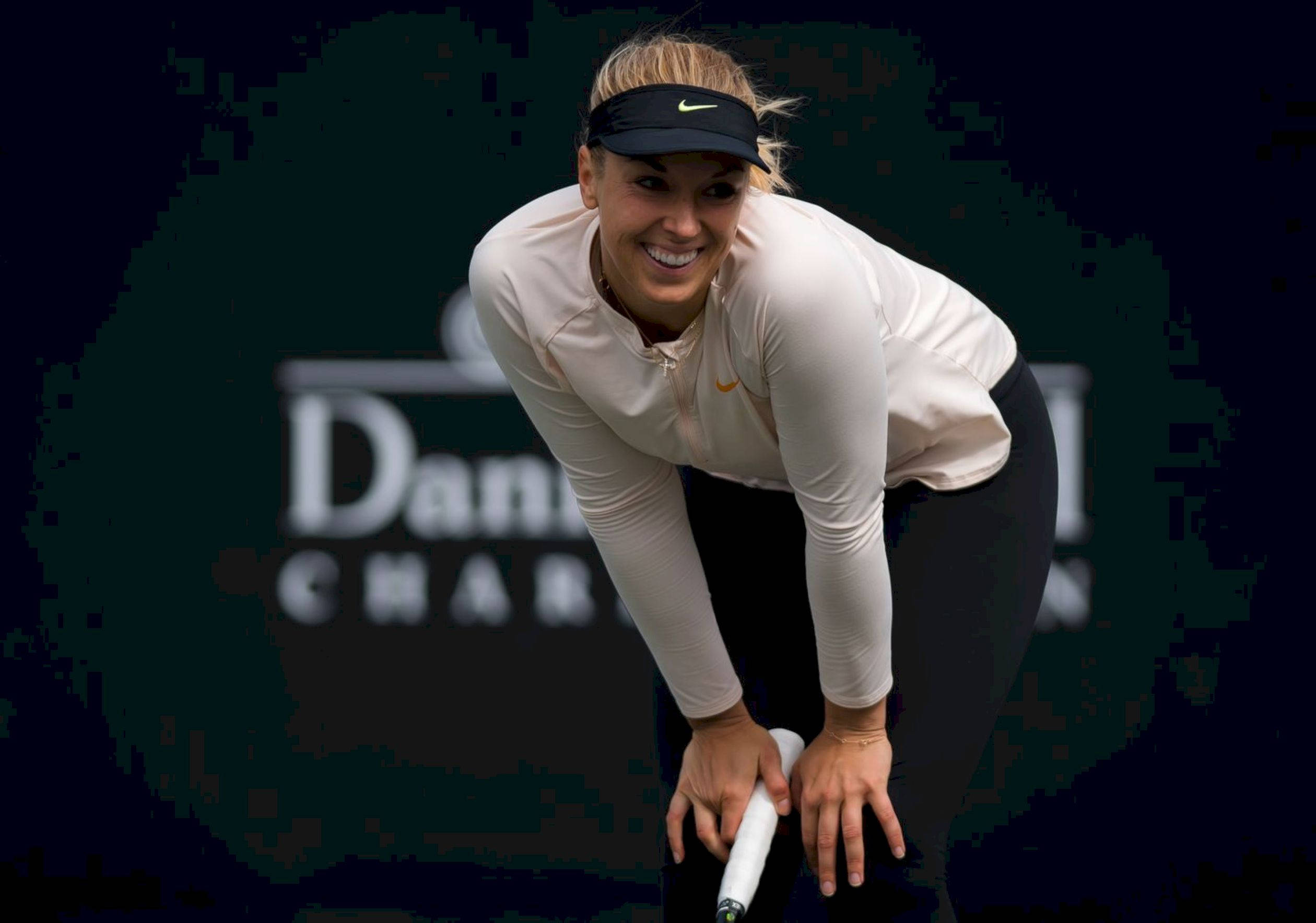 Tennis 桌布 壁紙 — 一位微笑的女網球選手向前彎腰，握著球拍，背景是模糊的深色球場。
