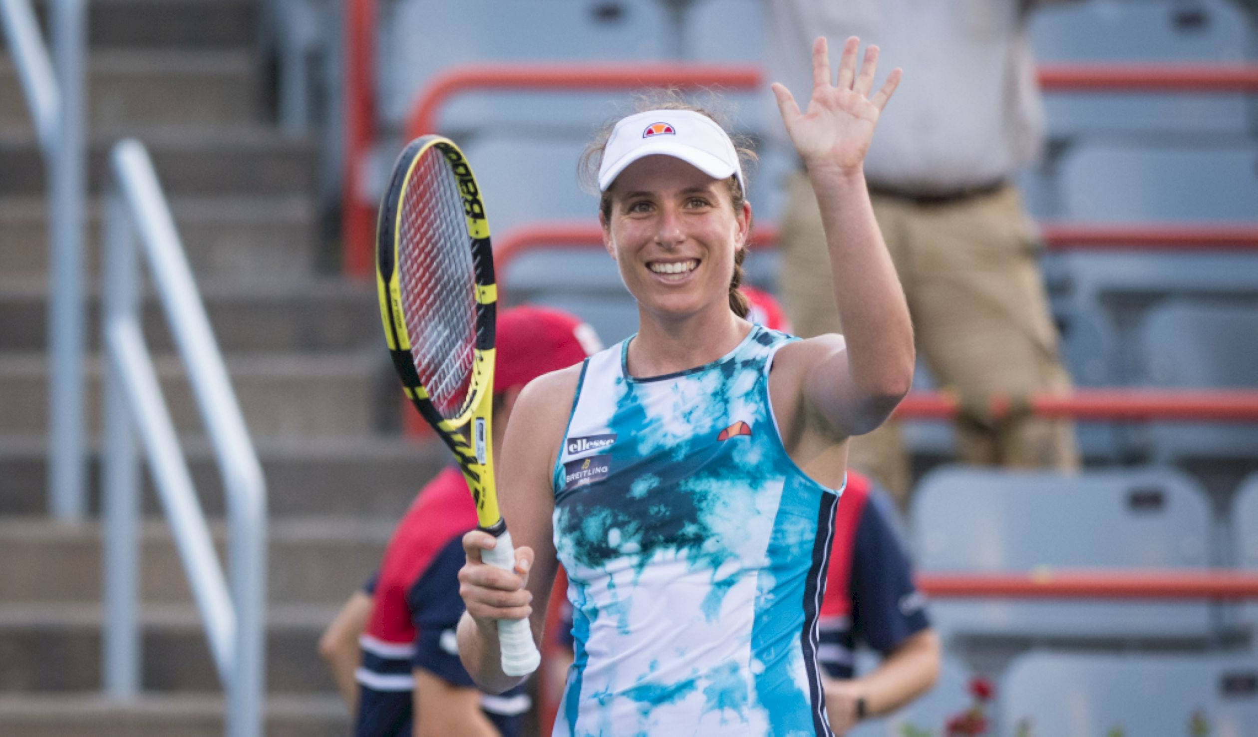 運動 桌布 壁紙 — 一位微笑的女網球選手在戶外球場上向粉絲揮手，手持黃黑相間的球拍。