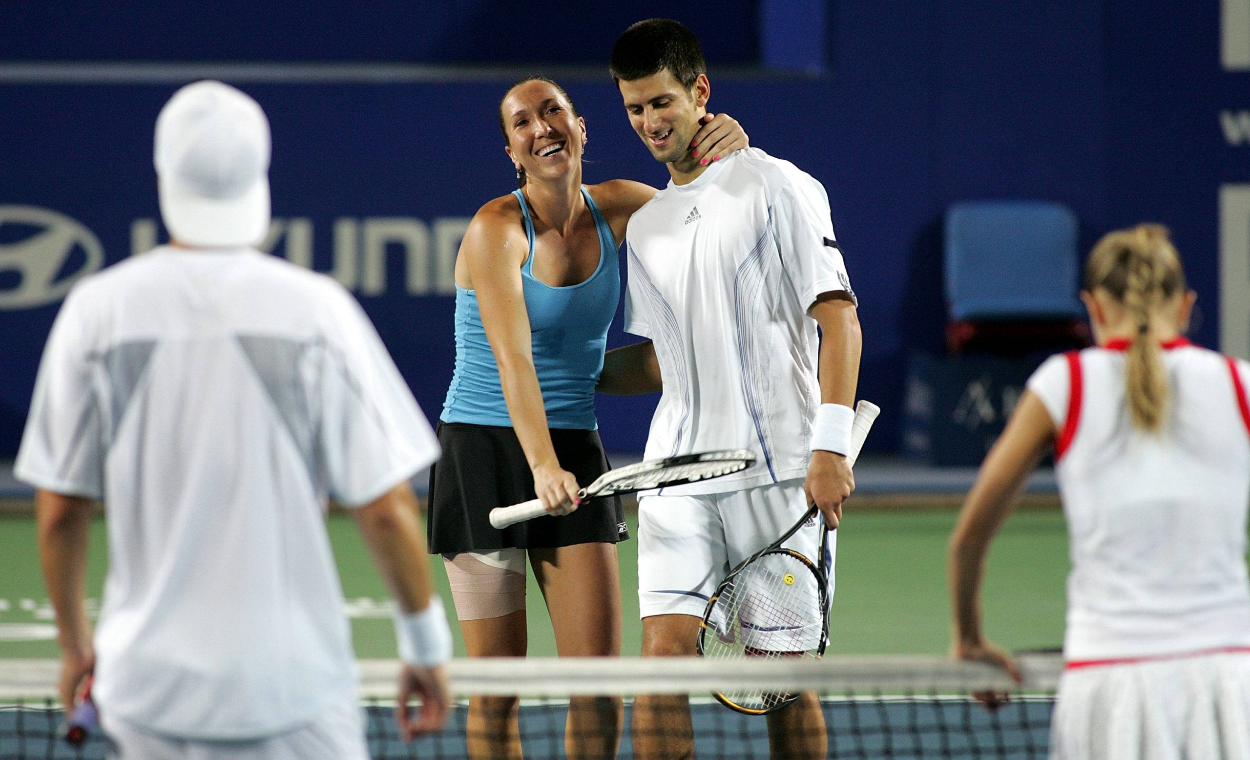 Tennis 桌布 壁紙 — 一位微笑的女網球選手在燈光明亮的球場上擁抱一位男選手，其他人站在附近。