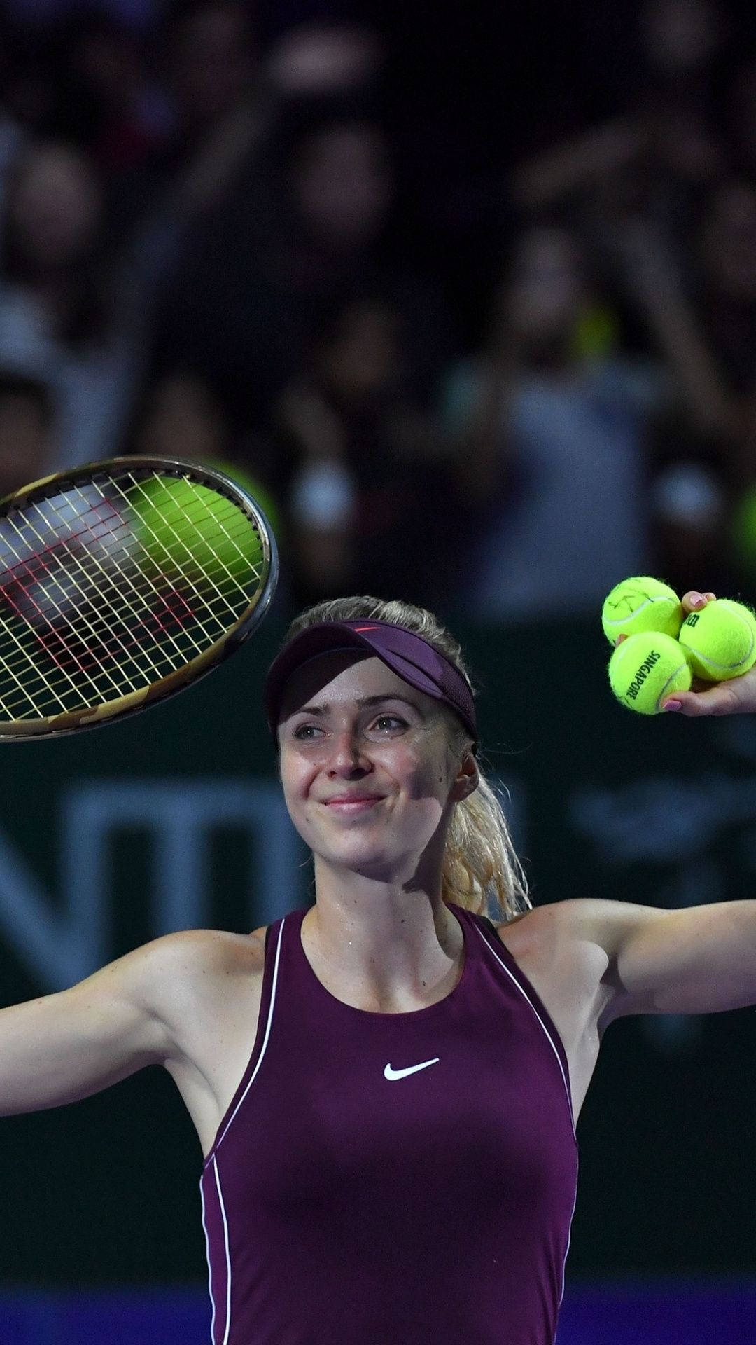 Athlete 桌布 壁紙 — 一位微笑的女網球選手穿著酒紅色服裝，在燈光明亮的球場上手持球拍和三顆亮黃色的球。