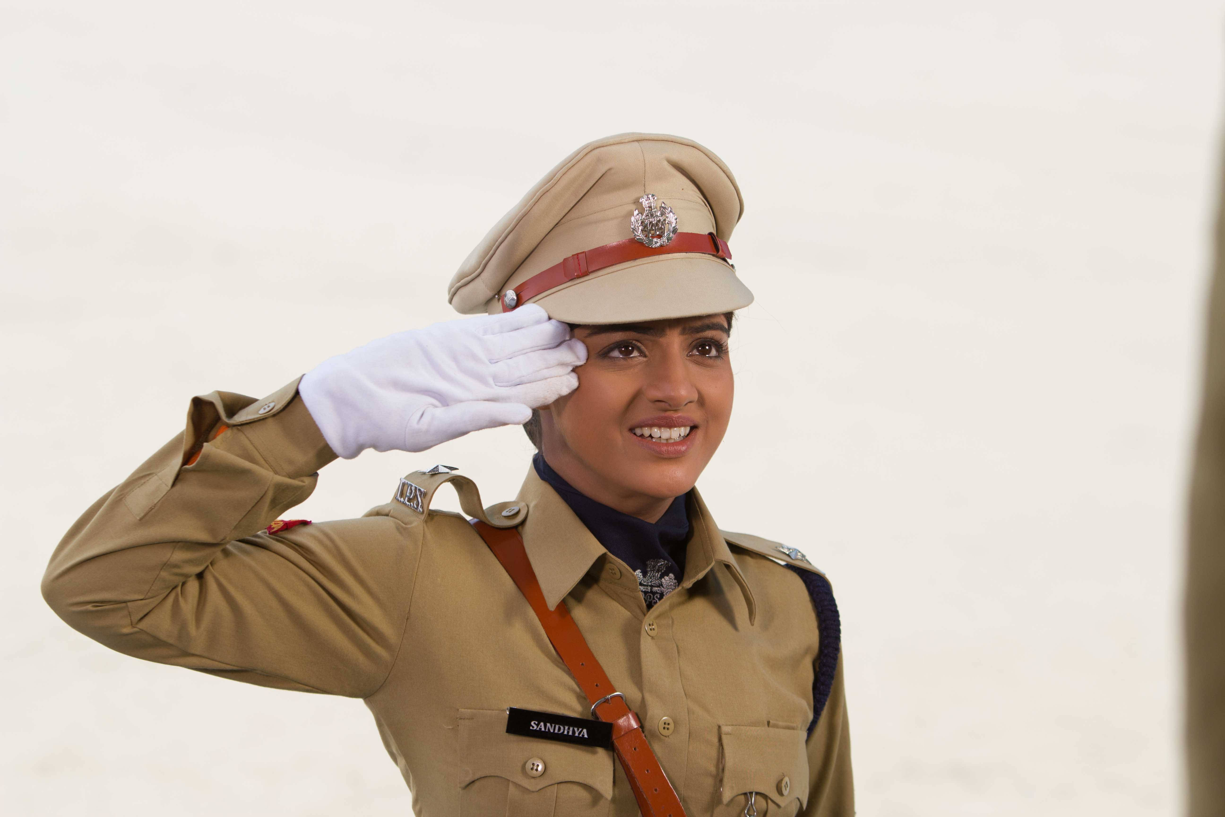 Indian 桌布 壁紙 — 一位微笑的女警穿著卡其色制服，戴著白手套敬禮，背景是純白色。