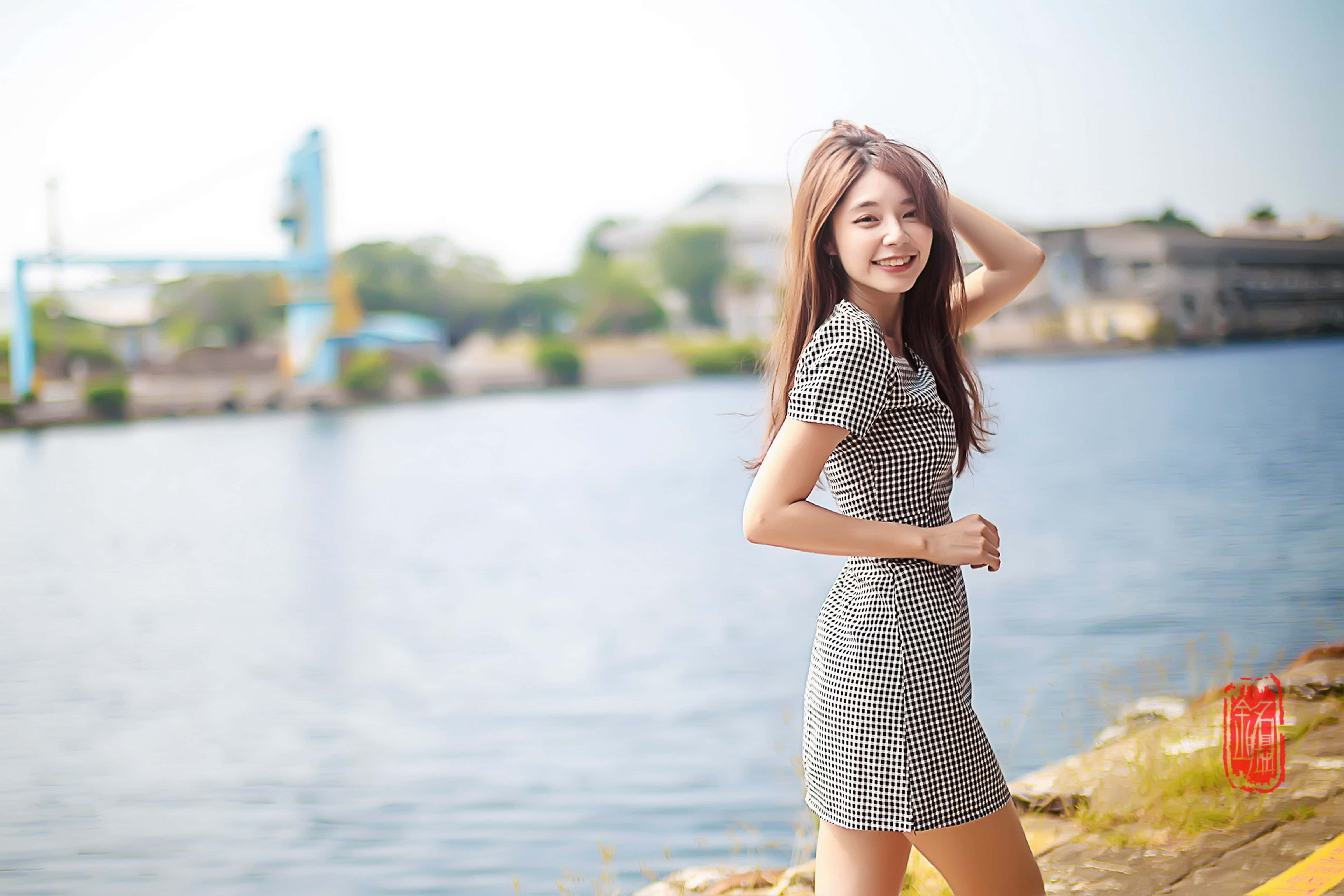 lovely girl 桌布 壁紙 — 一位微笑的年輕女士穿著黑白格紋連衣裙，在陽光明媚的日子裡站在平靜的河邊。