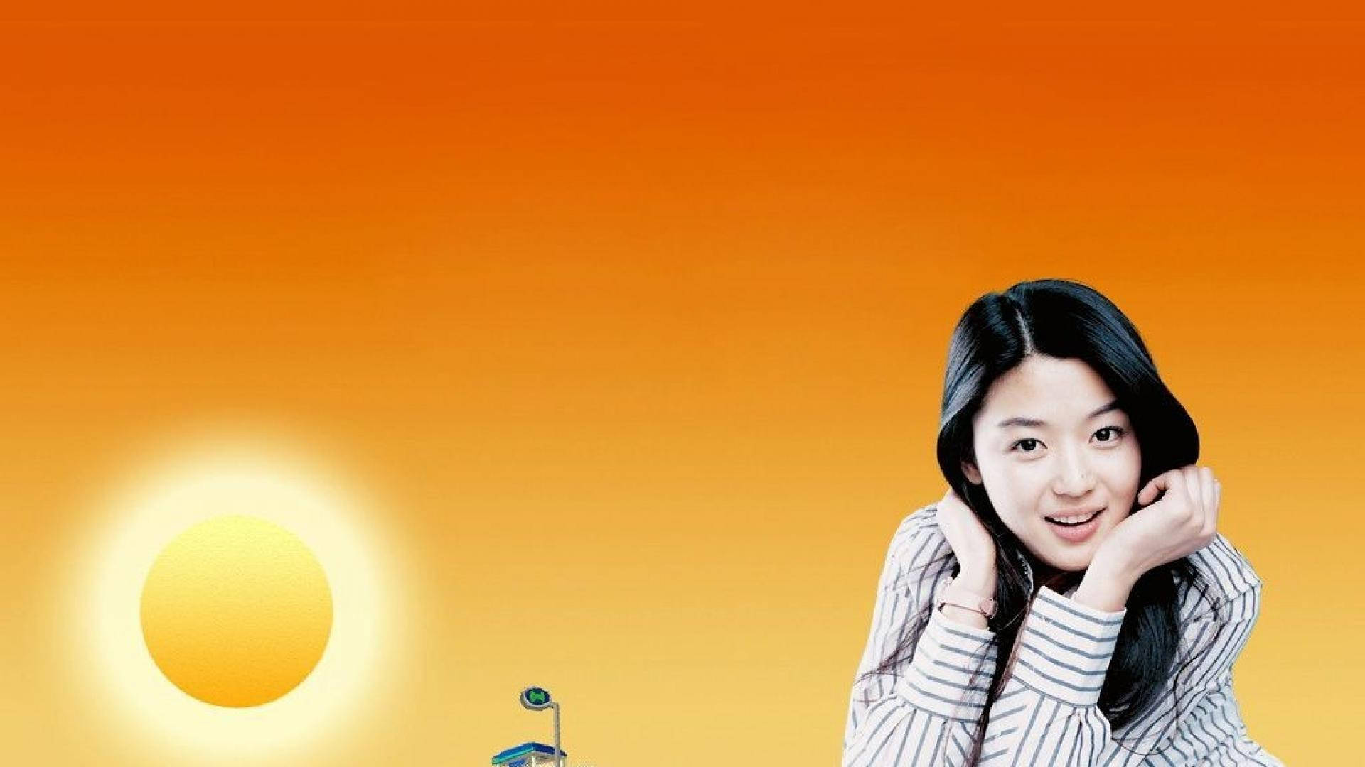 Jun Ji Hyun 桌布 壁紙 — 一位微笑的年輕女子將下巴擱在手上，背景是充滿活力的橙色日落天空，太陽閃耀。