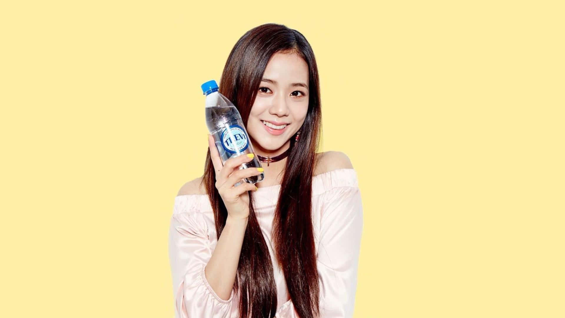 BLACKPINK 桌布 壁紙 — 一位微笑的年輕女性，長長的黑髮，在純淡黃色背景前拿著一瓶清澈的飲料。