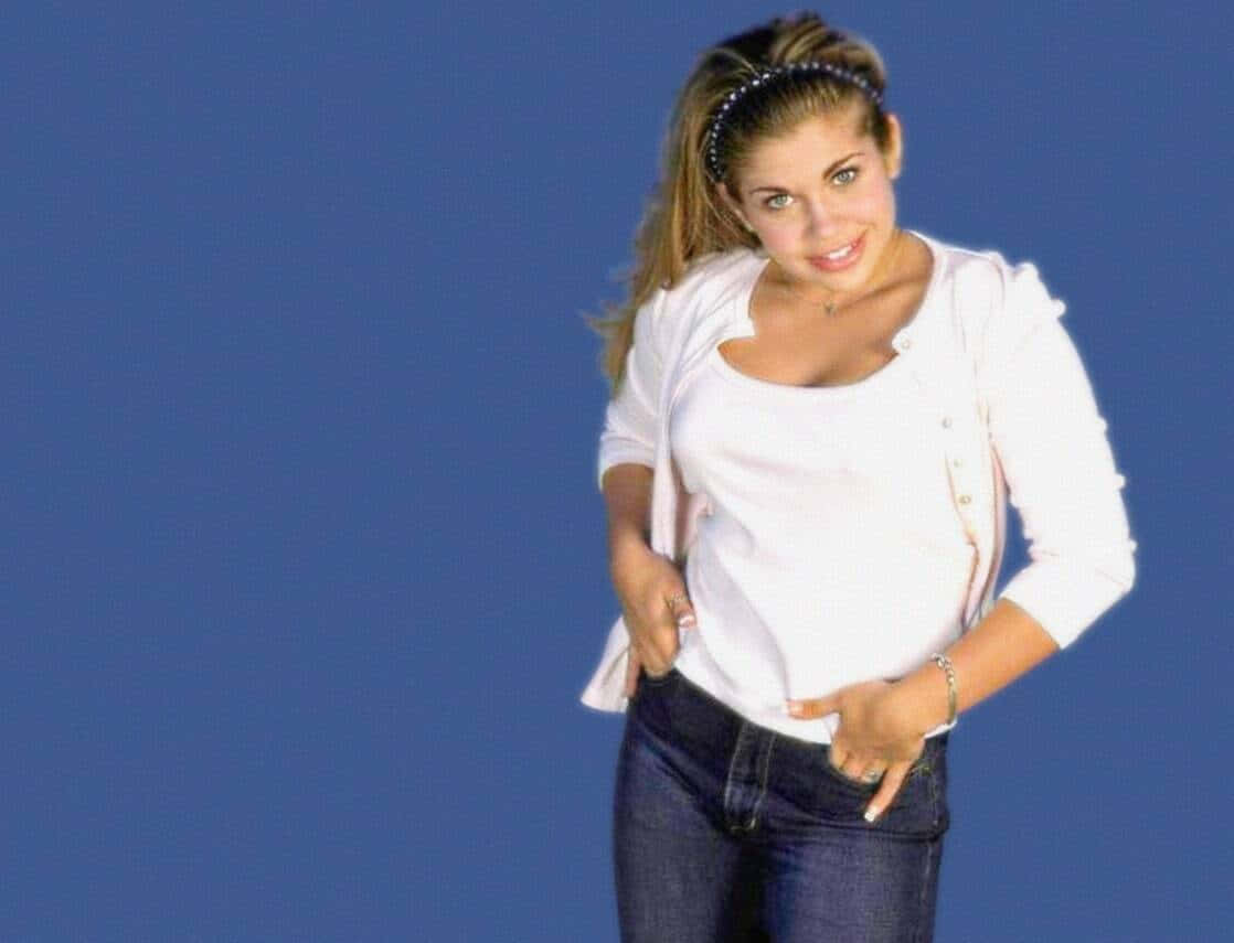 Danielle Fishel 桌布 壁紙 — 一位微笑的年輕女性身穿白色上衣和牛仔褲，在純藍色攝影棚背景前自信地擺姿勢。