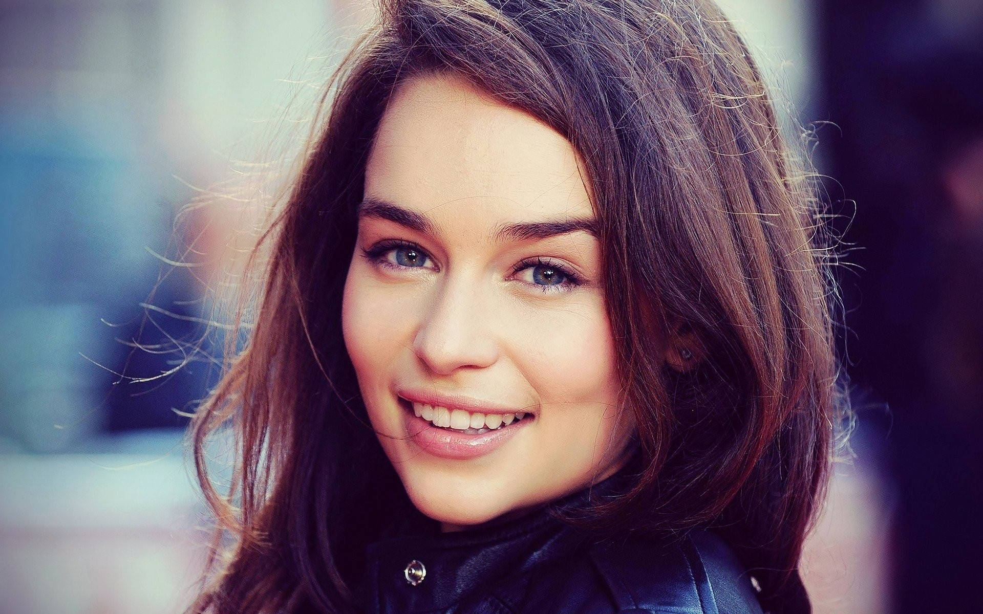 Emilia 桌布 壁紙 — 一位微笑的年輕女性近距離肖像，棕色頭髮，藍色眼睛，穿著黑色皮夾克。