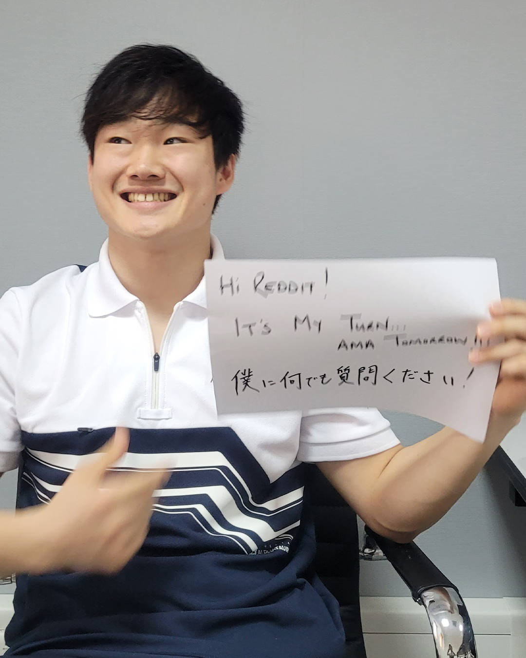 Smile 桌布 壁紙 — 一位微笑的年輕男子穿著條紋Polo衫，手持手寫標語向Reddit打招呼並邀請提問。