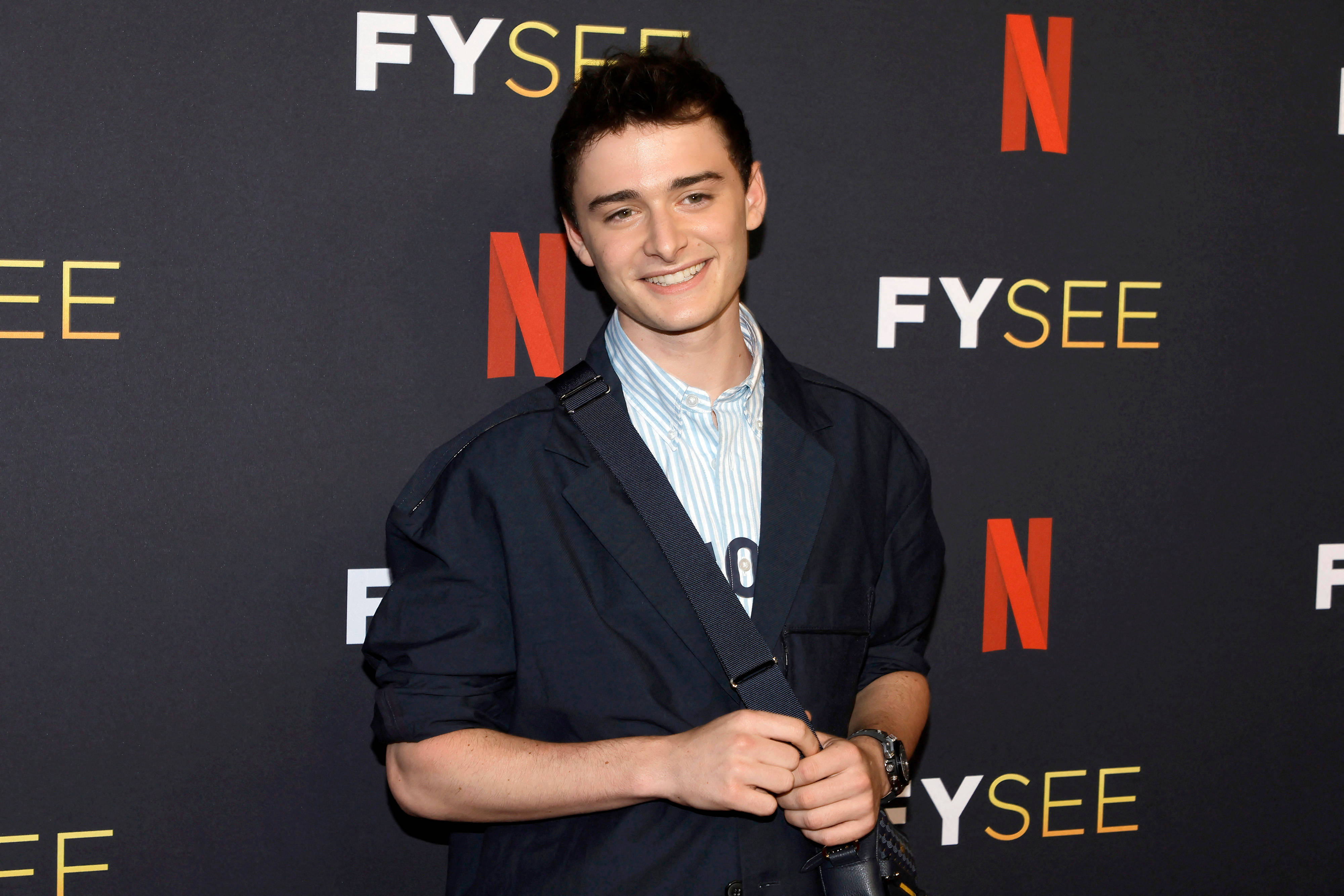 Netflix 桌布 壁紙 — 一位微笑的年輕男子身穿海軍藍外套，在Netflix FYSEE活動中自信地站在品牌背景前。