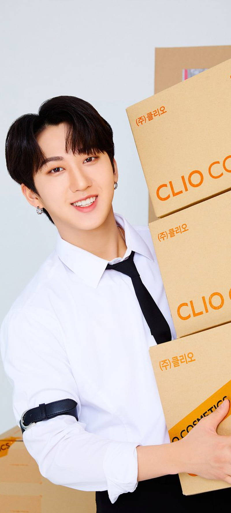 Changbin 桌布 壁紙 — 一位微笑的年輕男子身穿白襯衫和黑領帶，在白色背景前拿著疊放的CLIO化妝品盒。
