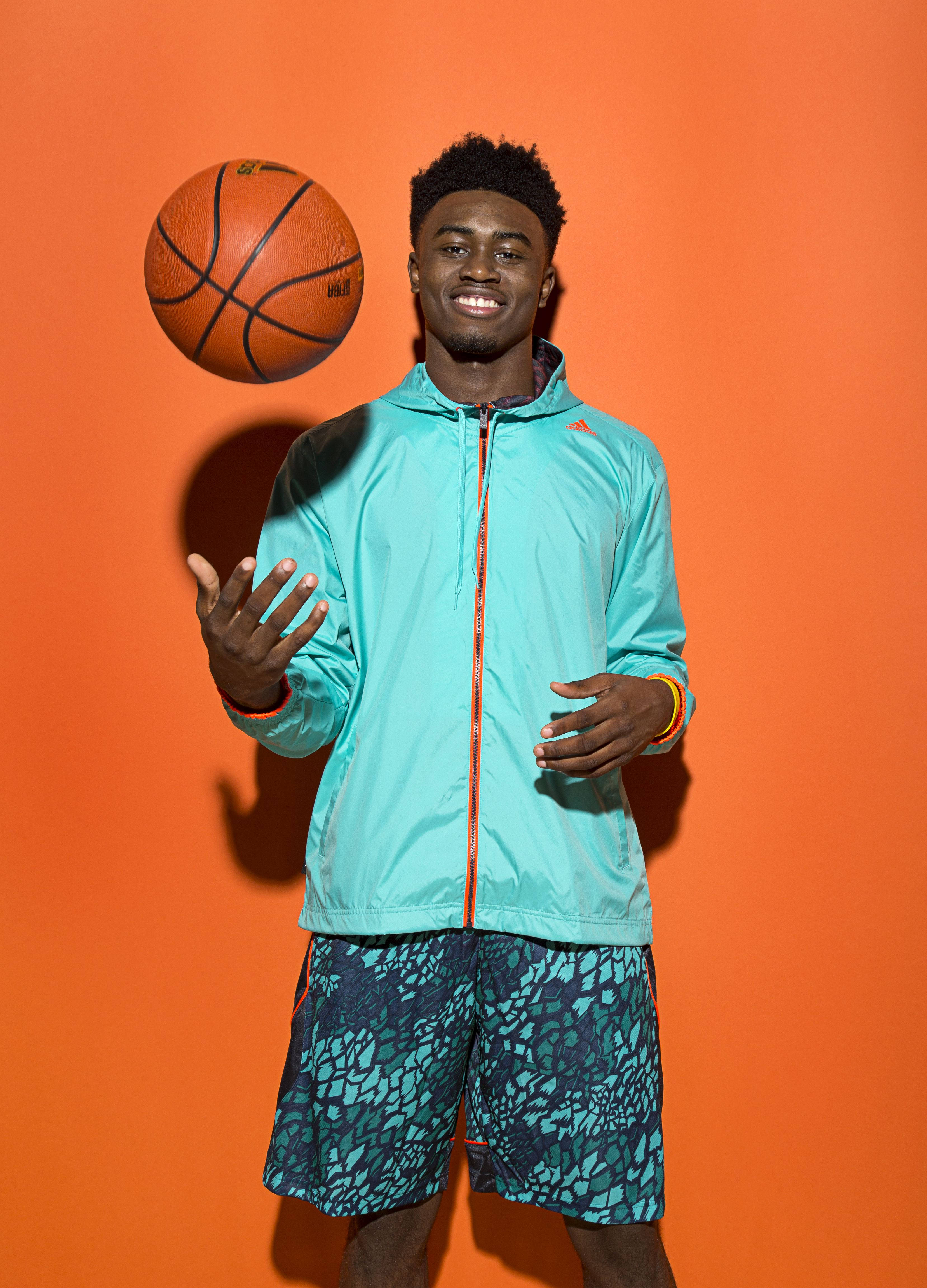 Jaylen Brown 桌布 壁紙 — 一位微笑的年輕男子身穿青綠色外套和圖案短褲，在充滿活力的橙色工作室背景前玩籃球雜耍。