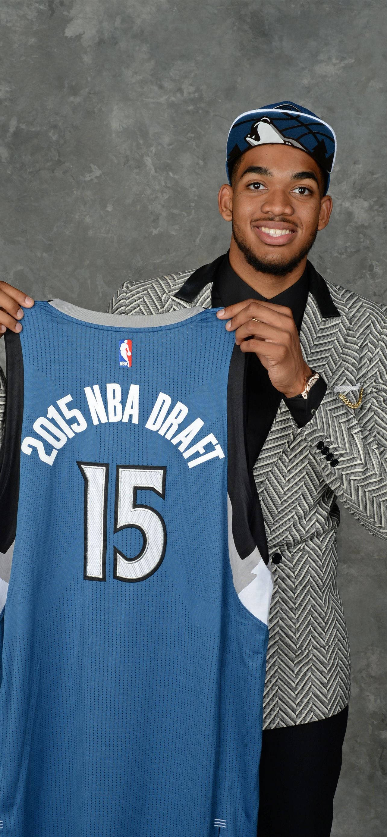 karl-anthony towns 桌布 壁紙 — 一位微笑的年輕籃球運動員自豪地舉起他的2015年NBA選秀球衣15號，背景是灰色攝影棚。