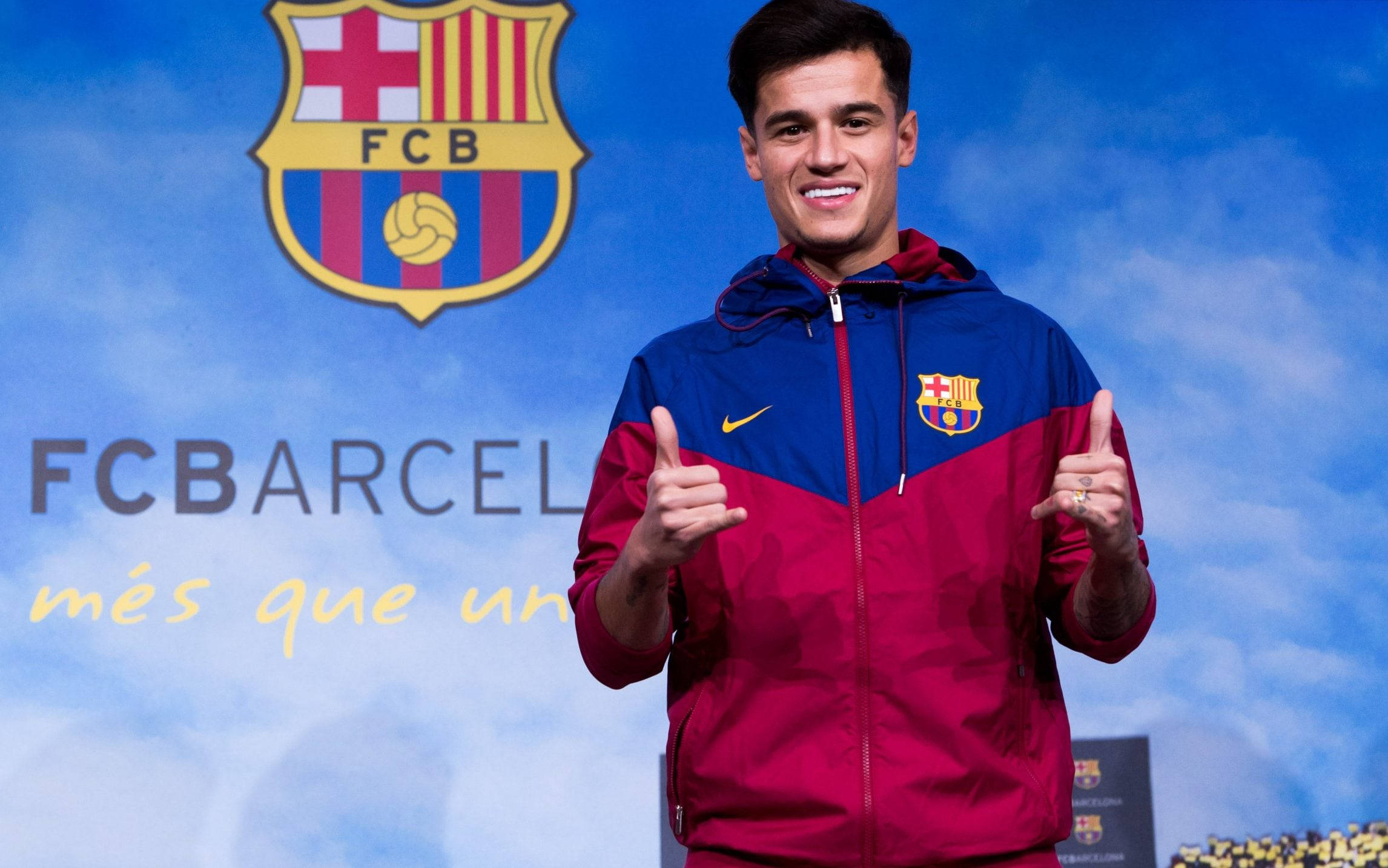 Coutinho 桌布 壁紙 — 一位微笑的年輕足球員穿著紅藍色的巴塞隆納俱樂部外套，在陰天背景下豎起兩個大拇指，並帶有俱樂部徽章。