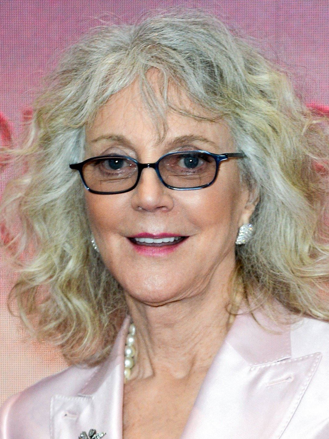 Celebrity 桌布 壁紙 — 一位微笑的年長女士的頭像特寫，她有一頭灰色捲髮，戴著眼鏡，身穿粉紅色緞面外套。