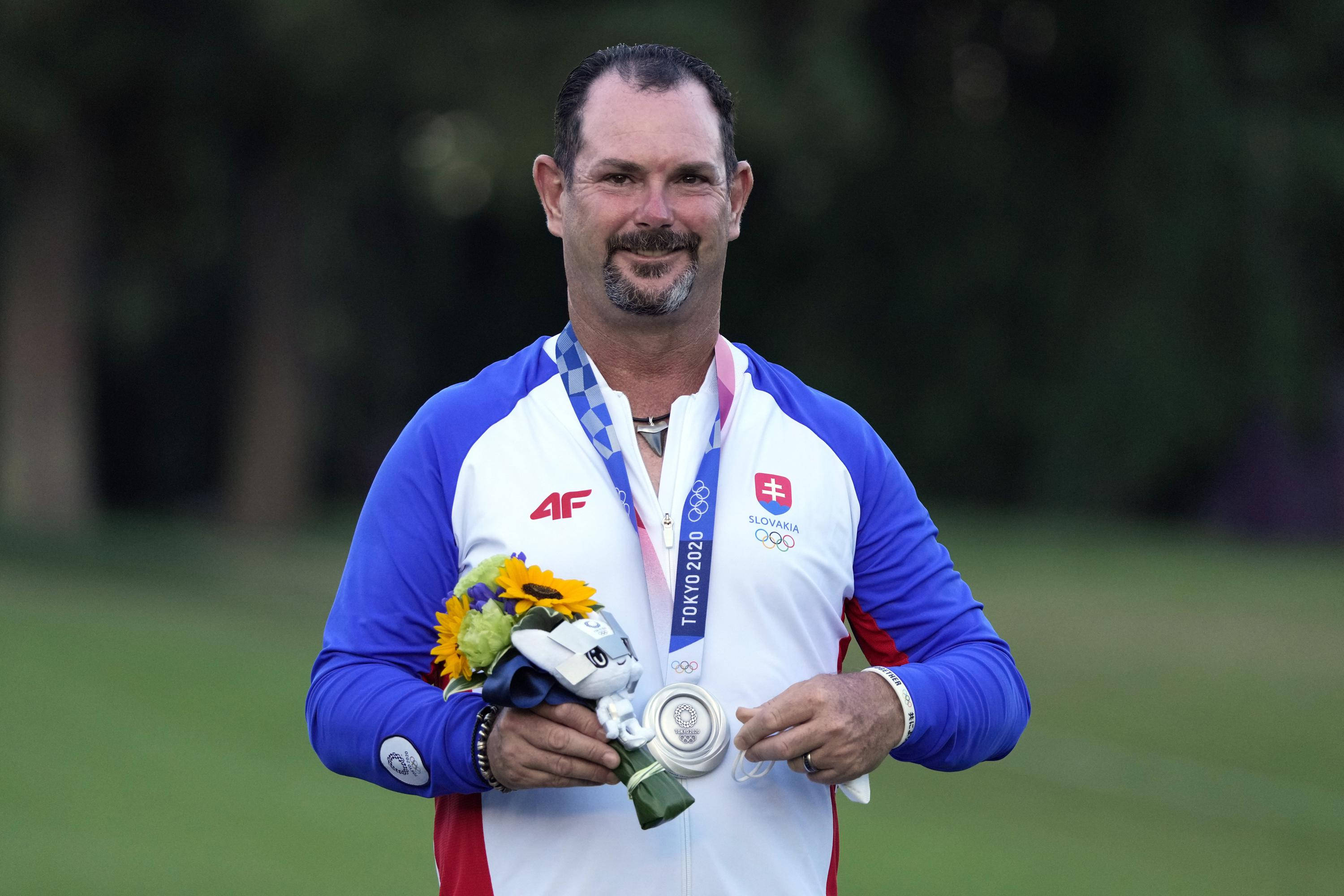 Athlete 桌布 壁紙 — 一位微笑的斯洛伐克高爾夫球手在綠色高爾夫球場上自豪地展示他的銀色奧運獎牌和色彩繽紛的花束。