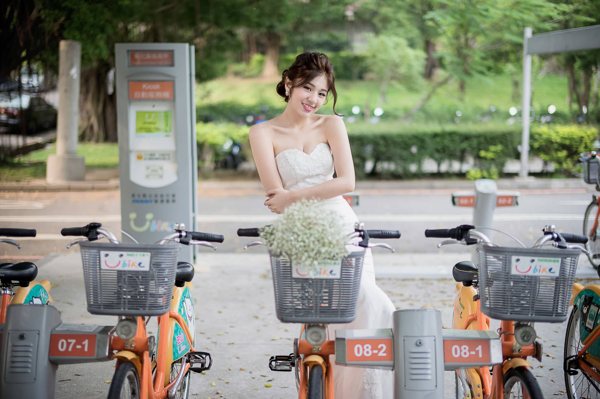 Bride 桌布 壁紙 — 一位微笑的新娘穿著白色禮服，靠在一排橙色出租腳踏車上，腳踏車籃裡有白色鮮花。