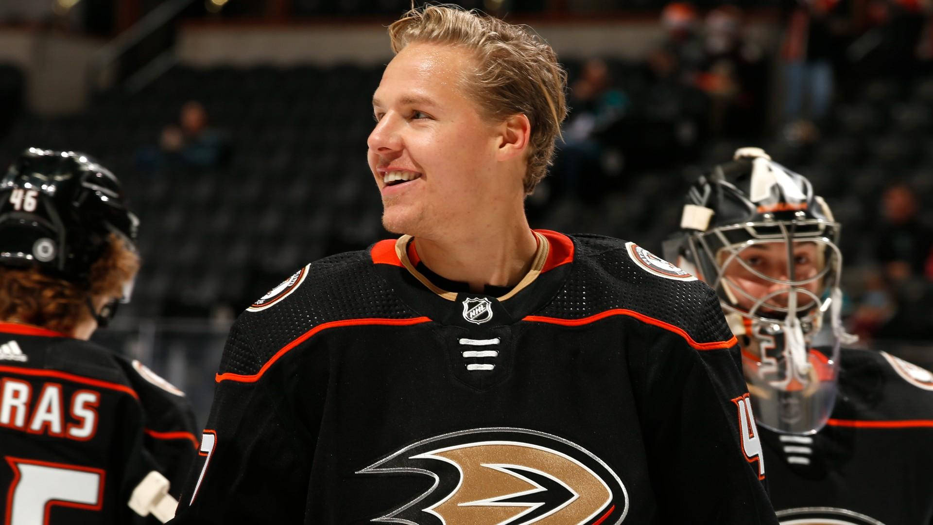 hockey 桌布 壁紙 — 一位微笑的曲棍球運動員穿著黑色Anaheim Ducks球衣，在比賽中與背景中的隊友一起大笑。